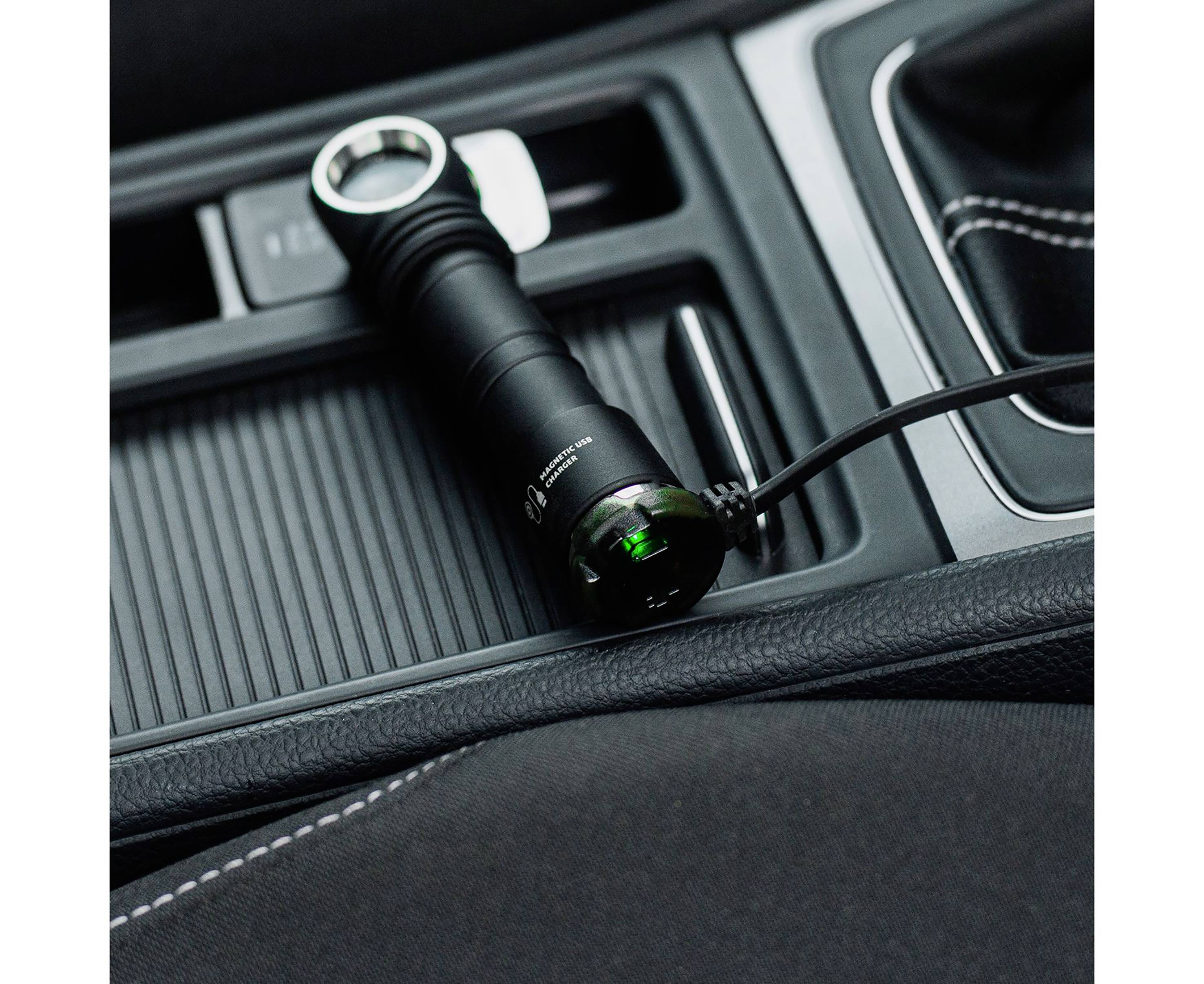 Taschenlampe wird im Auto aufgeladen. Sie liegt auf einer Mittelkonsole mit schwarzem Leder.
