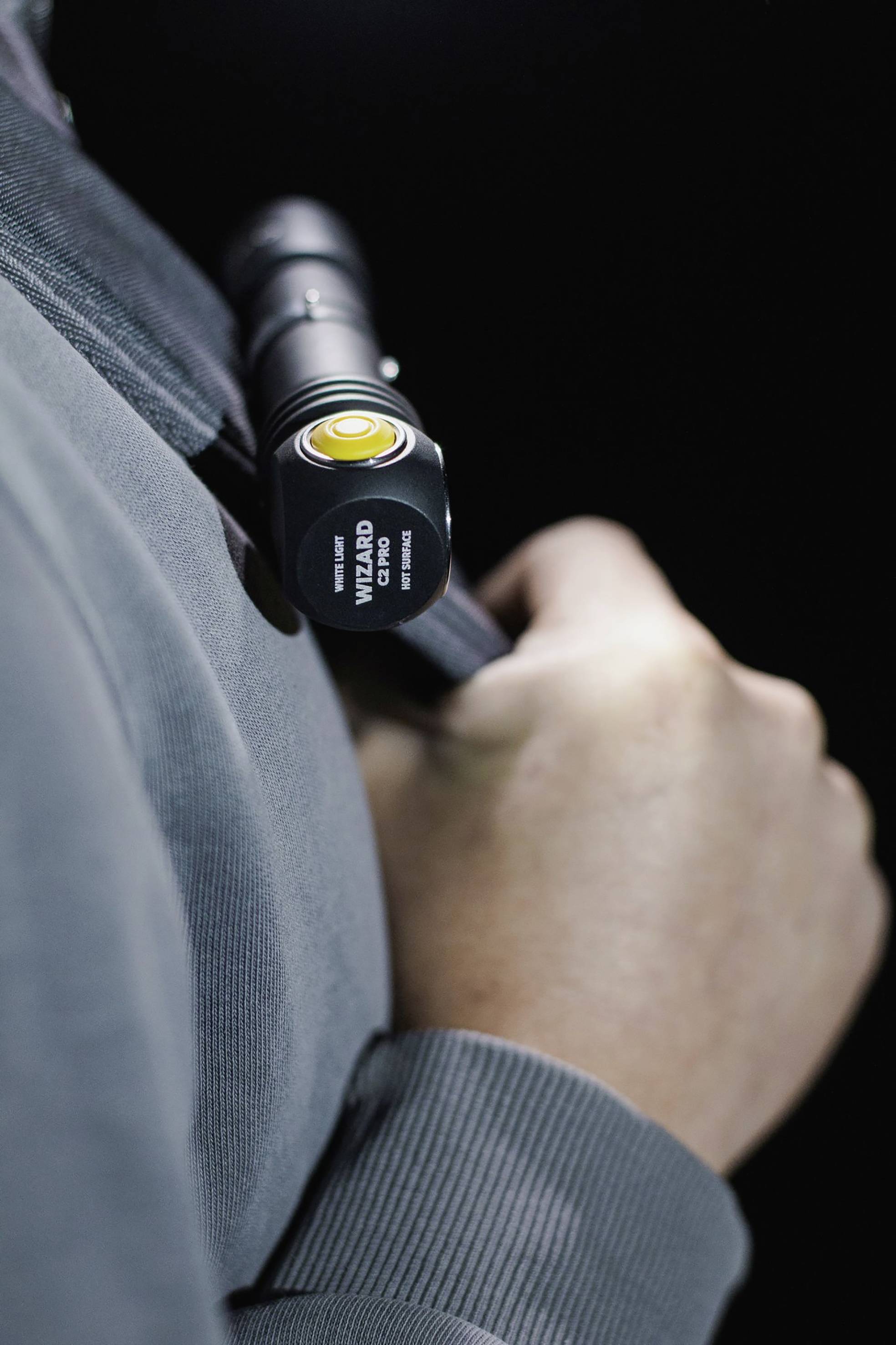 Person hält eine Taschenlampe an der Schulter. Die Taschenlampe zeigt nach vorne, und ein gelbes Lichtelement ist sichtbar.