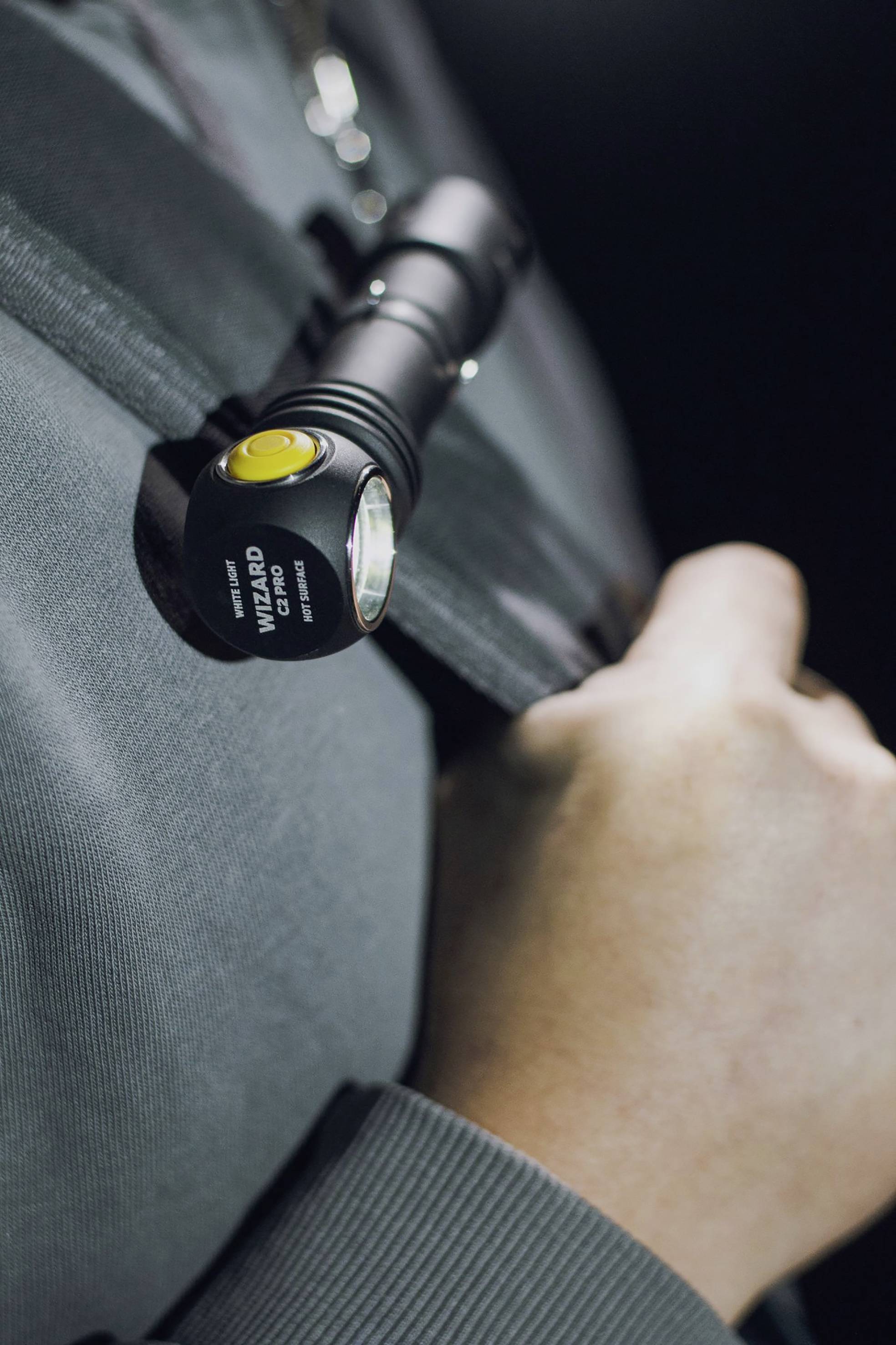 Eine Person trägt eine Taschenlampe an der Schulter, die an einem Rucksackriemen befestigt ist. Die Hand hält den Riemen.