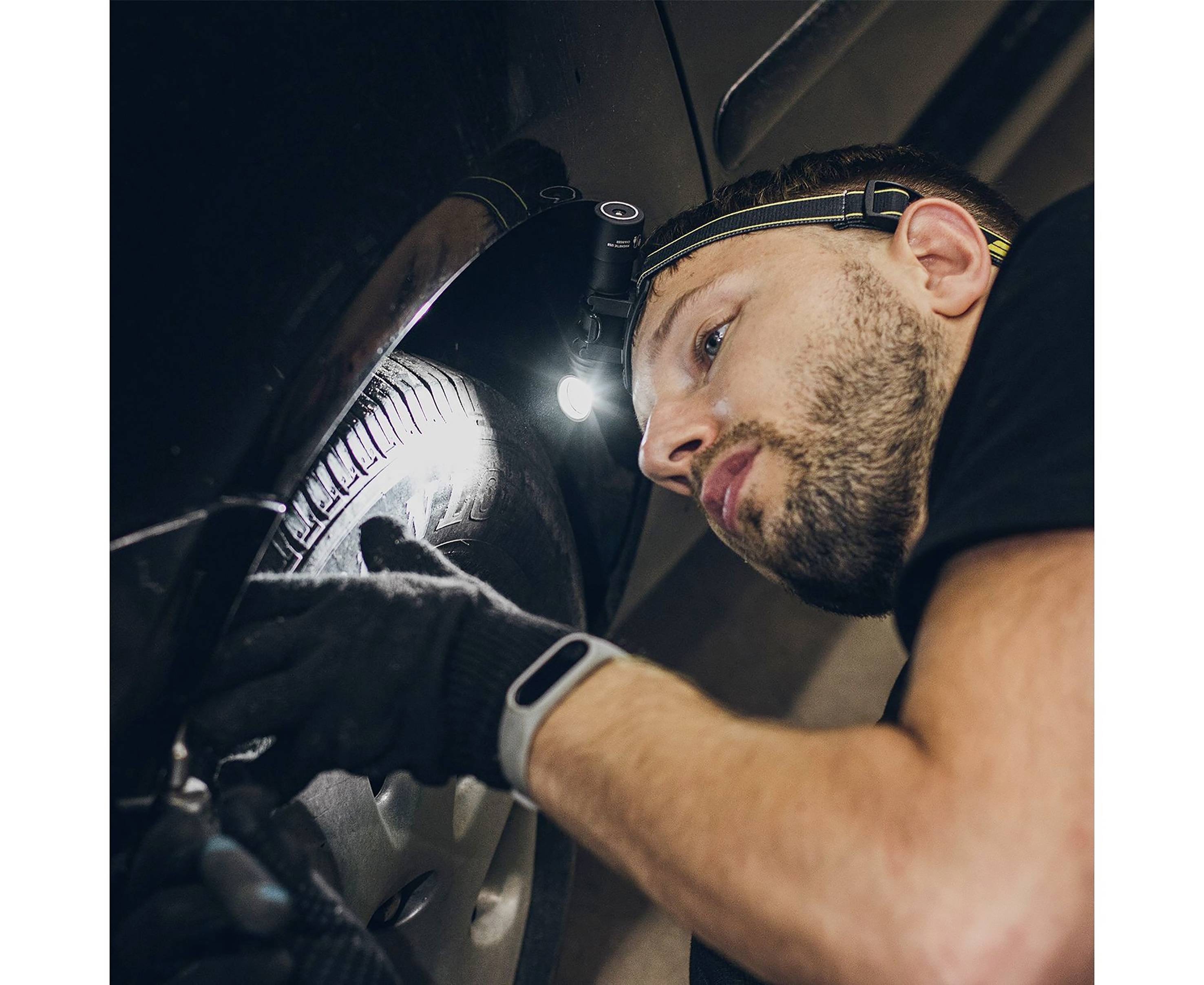 Mann mit Stirnlampe und Handschuhen inspiziert Autoreifen in einer Werkstatt.