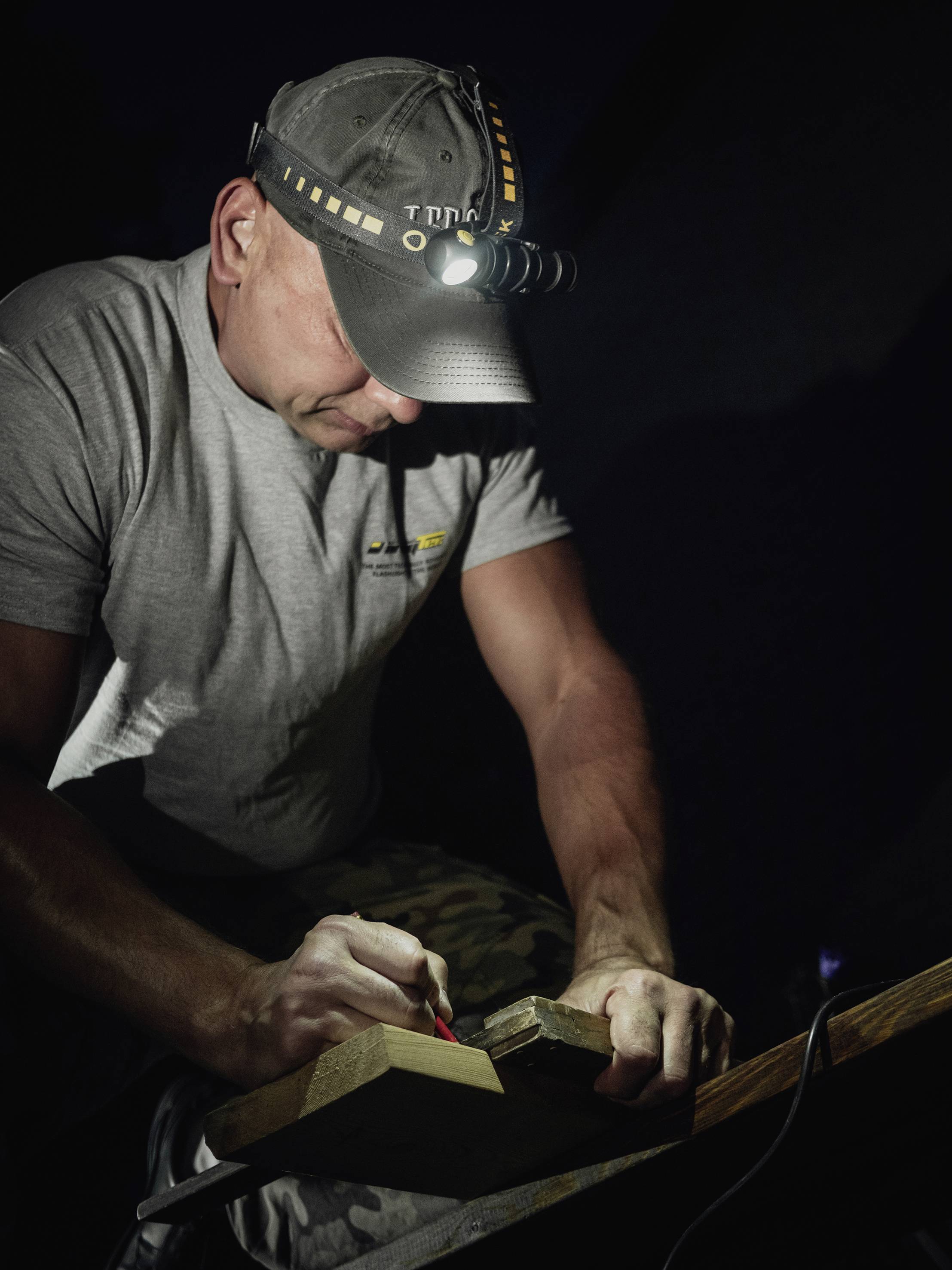Eine Person arbeitet in der Dunkelheit mit einer Taschenlampe auf der Mütze und bearbeitet vorsichtig ein Holzstück.