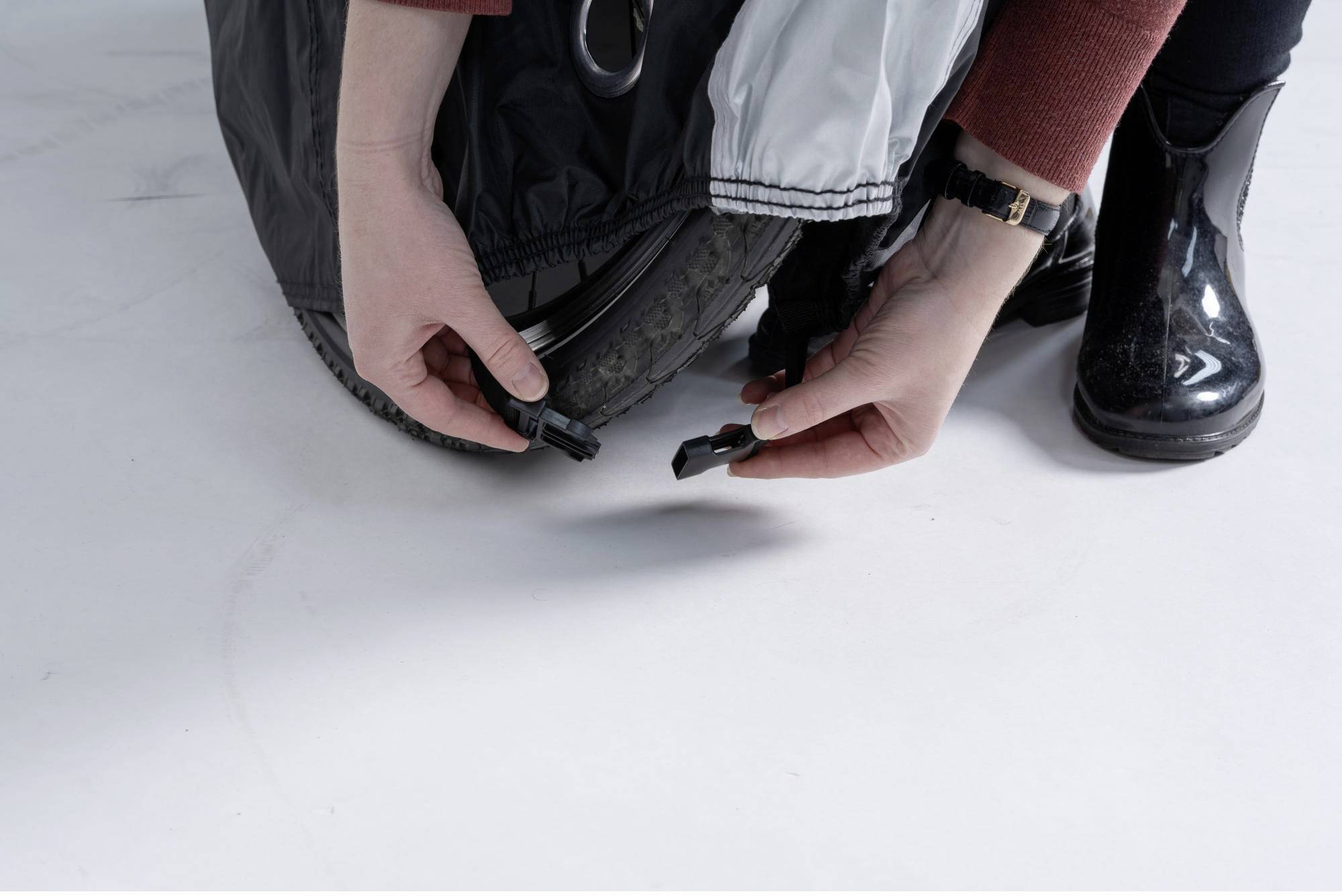 Eine Person befestigt eine schwarze Abdeckung an einem Rollstuhlrad mit einem Klickverschluss.