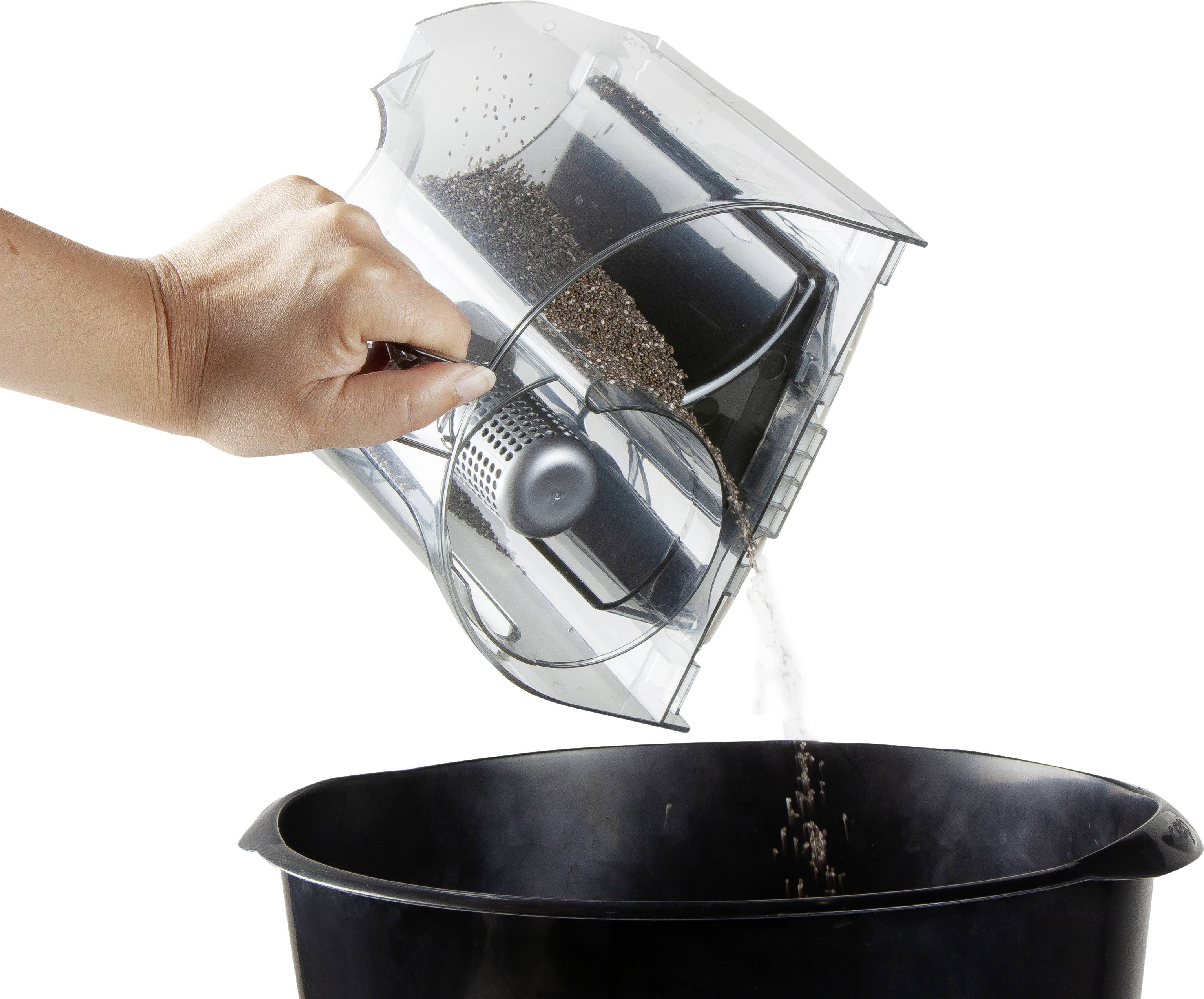 'Eine Hand leert einen Behälter mit Staub und Schmutz in einen schwarzen Mülleimer.'