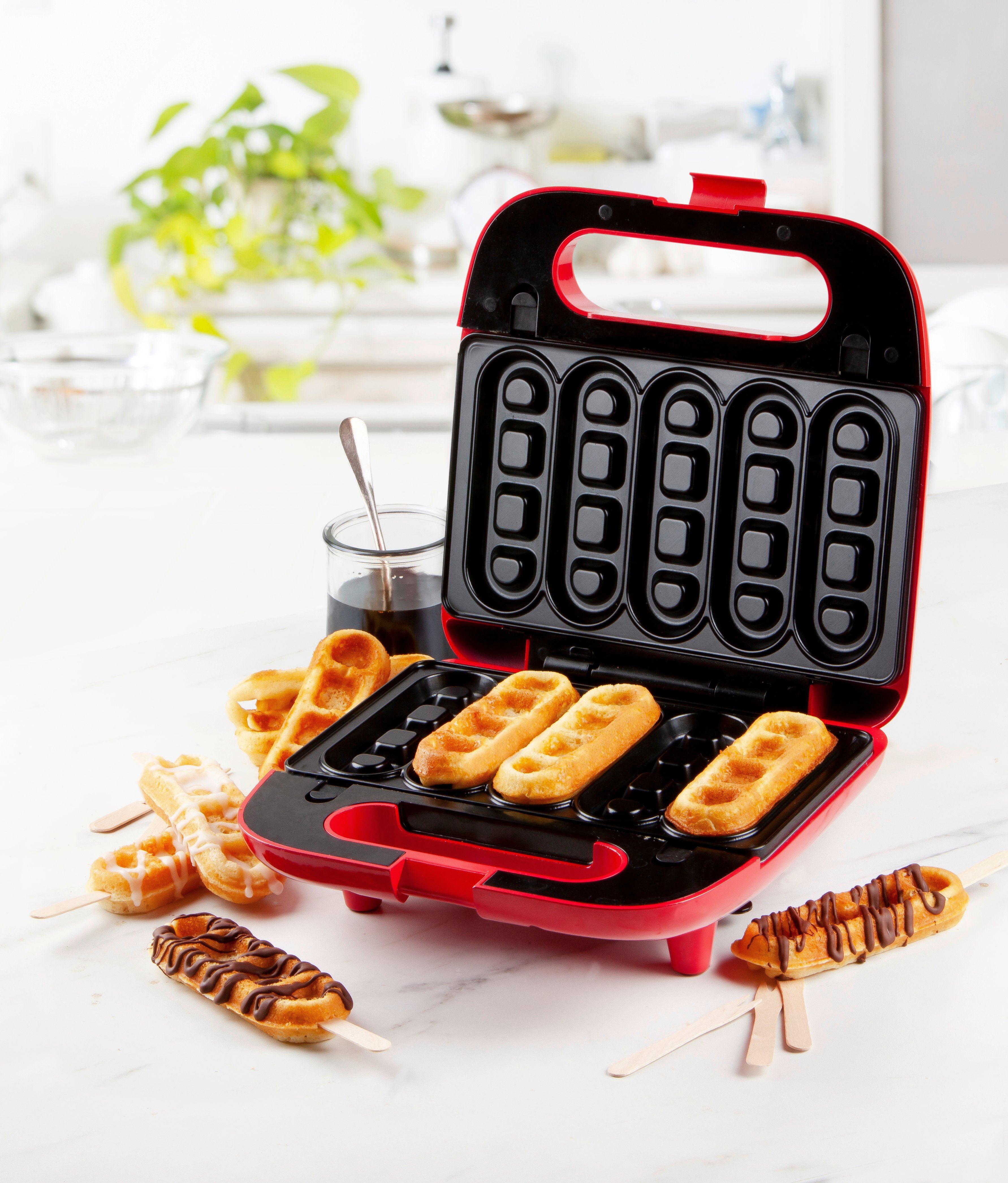 Waffelautomaten in einer Küche mit mehreren gebackenen Waffeln auf Stielen, einige mit Schokoladenglasur verziert.