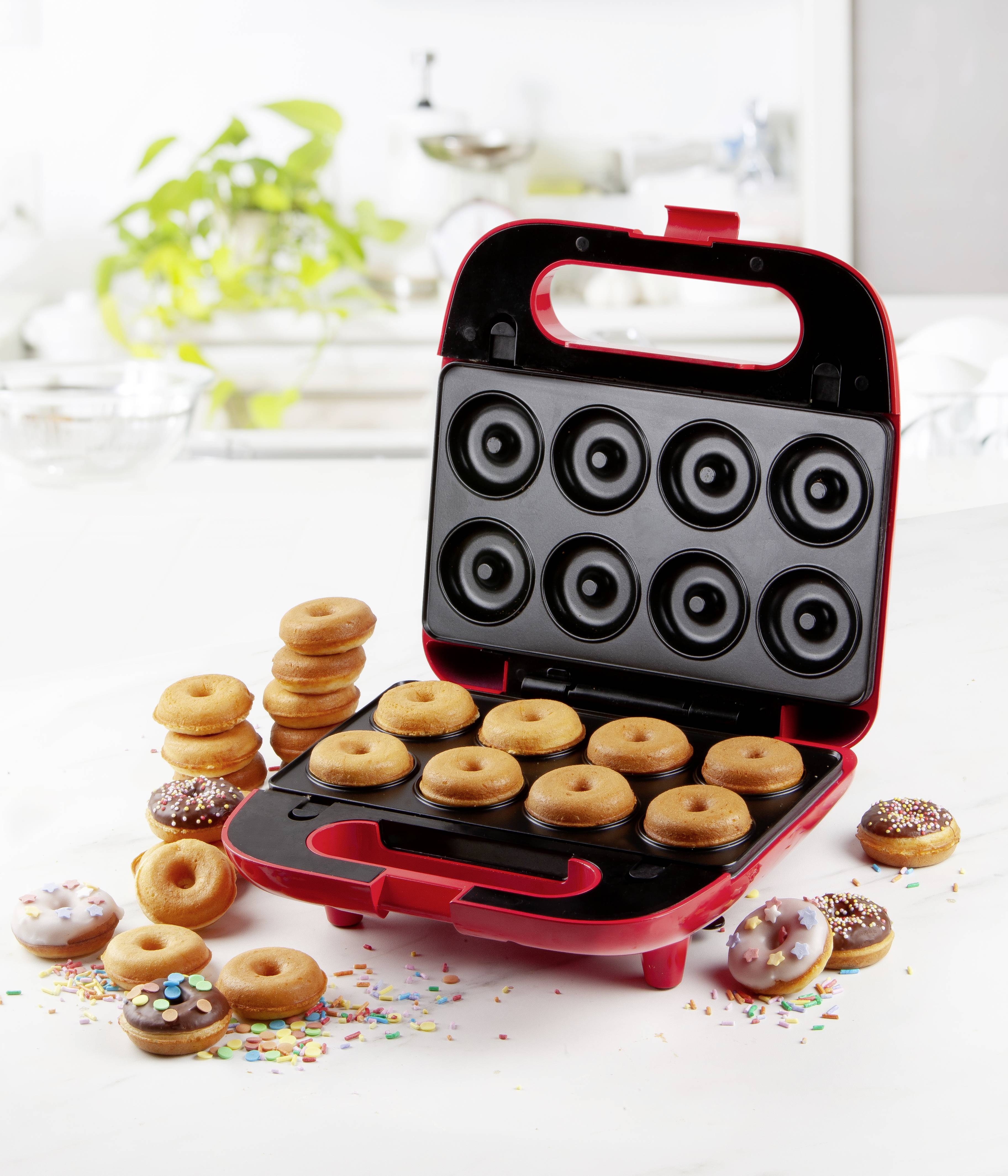 Mini-Donut-Maker auf Küchentresen, gefüllt mit frisch gebackenen Donuts. Einige Donuts dekoriert mit Zuckerglasur und Streuseln.