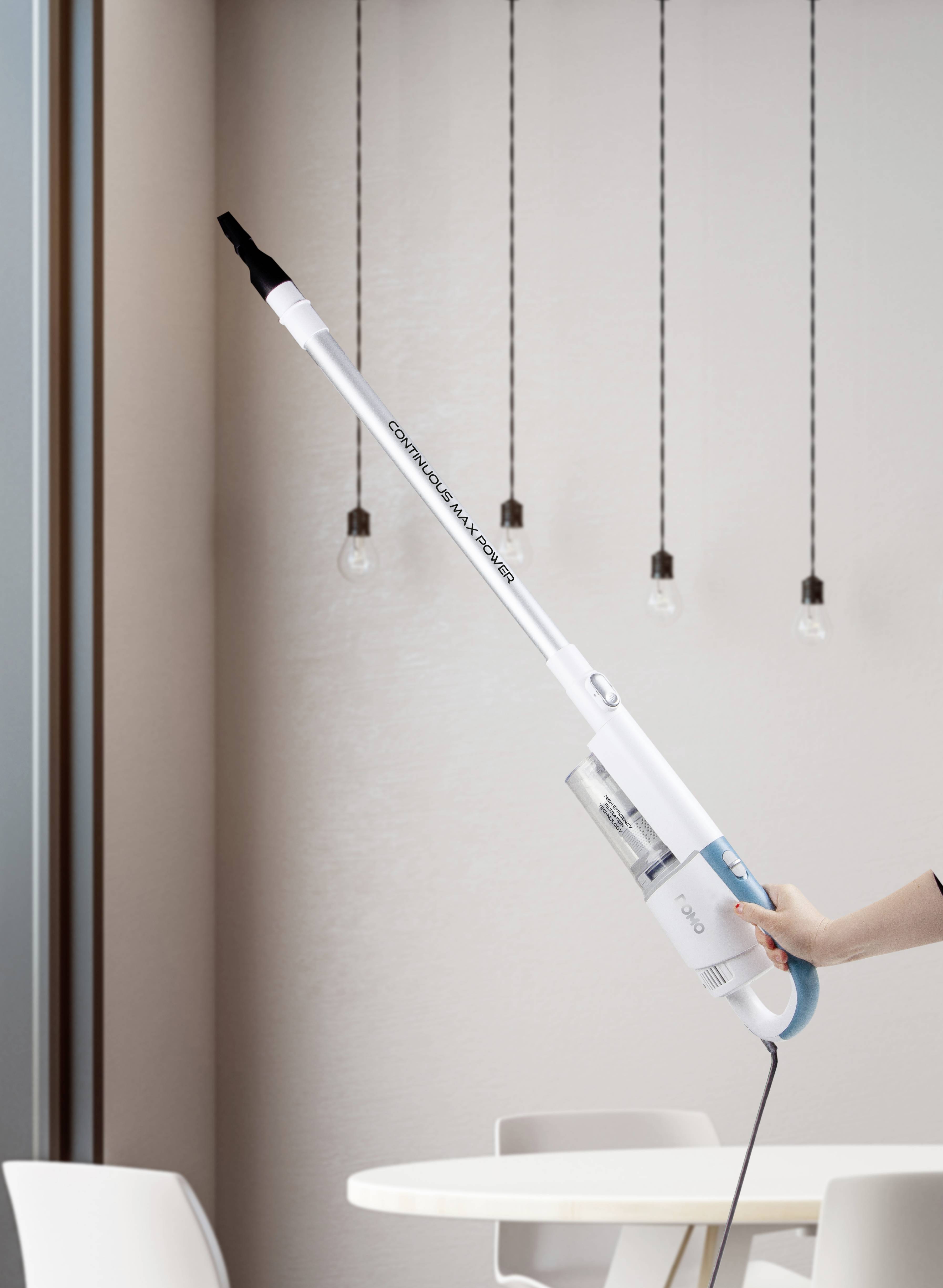 Eine Hand hält einen leichten, kabellosen Staubsauger, der aufrecht steht, mit einem modernen Wohnzimmerhintergrund und hängenden Lampen.