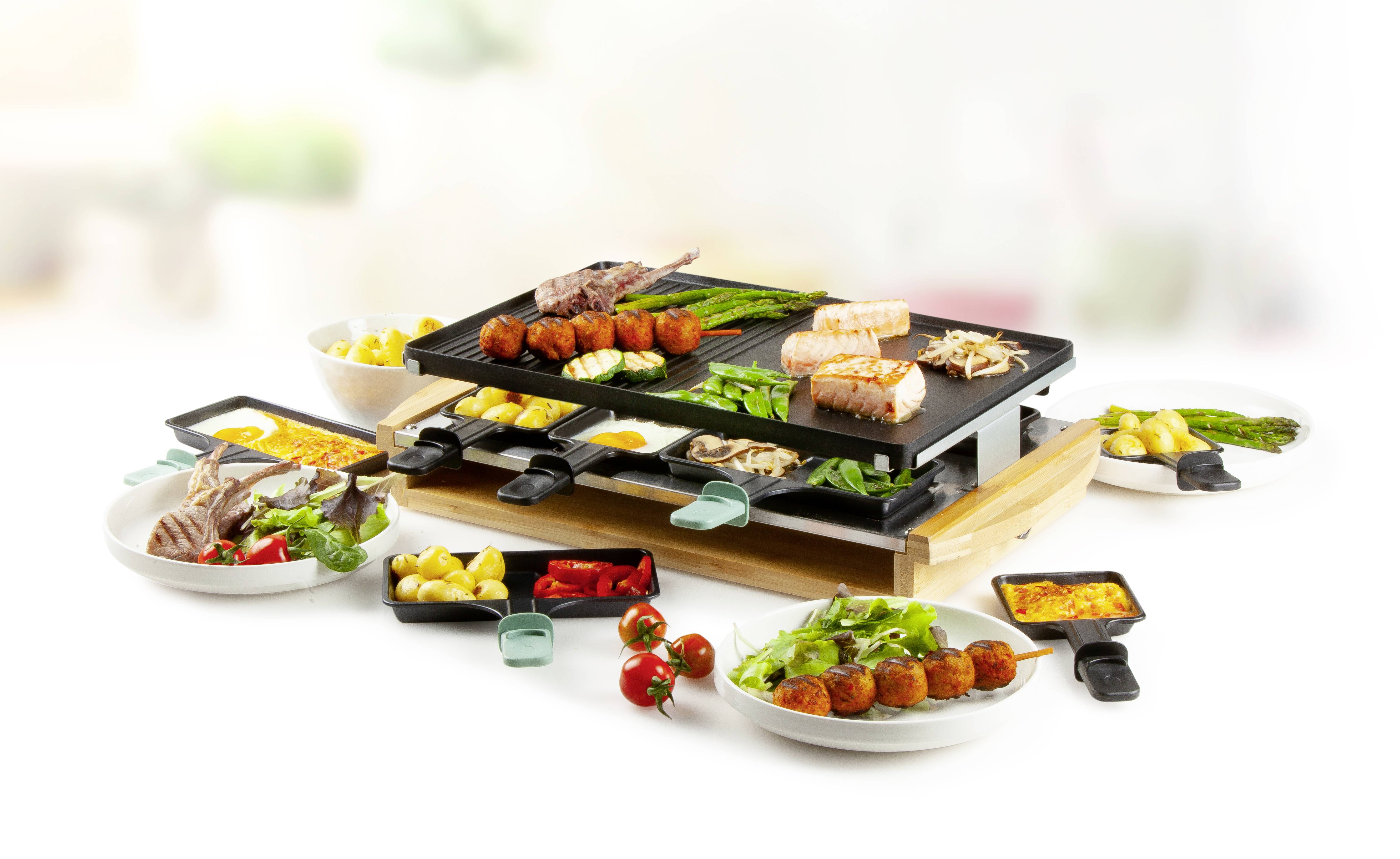 Ein Raclette-Grill mit verschiedenen Zutaten wie Fleisch, Gemüse und Käse. Rundherum liegen Schälchen mit weiteren Beilagen.