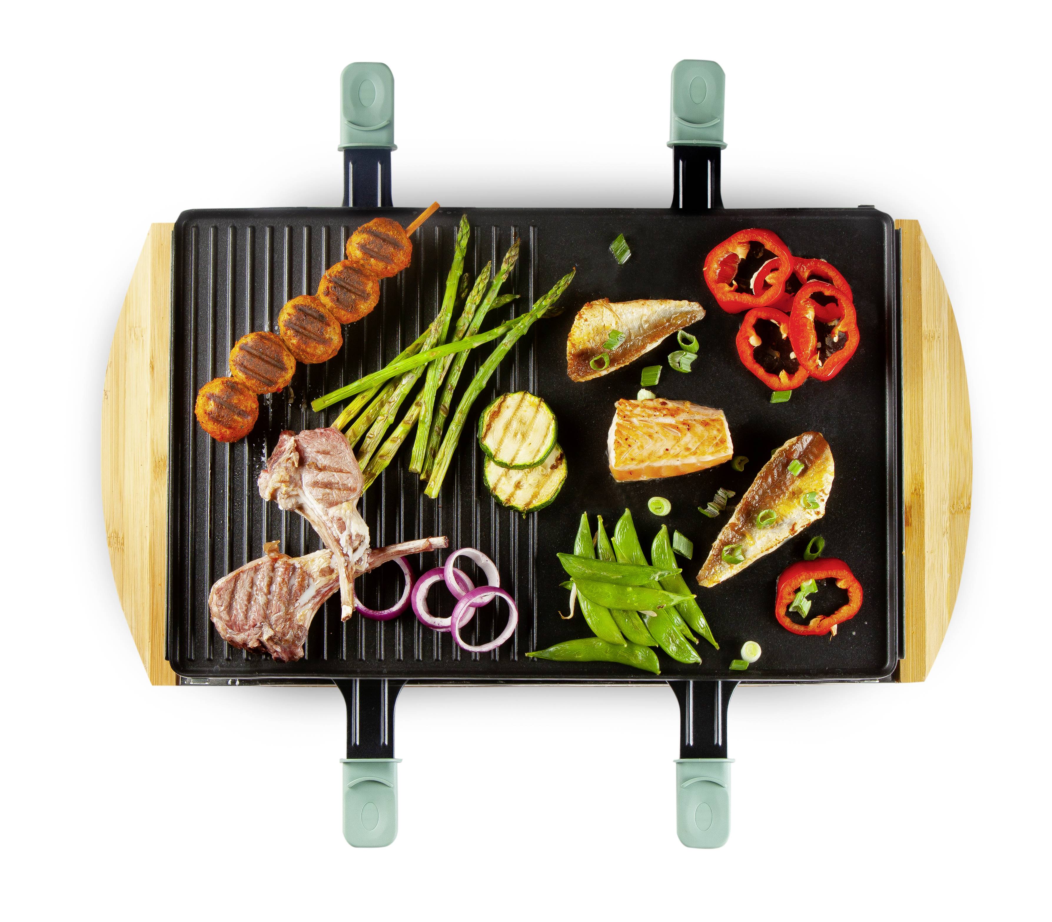 Ein Grill mit verschiedenen Lebensmitteln: Lammkoteletts, Lachs, Spargel, Paprika, Karotten am Spieß und Zwiebeln, von oben gesehen.