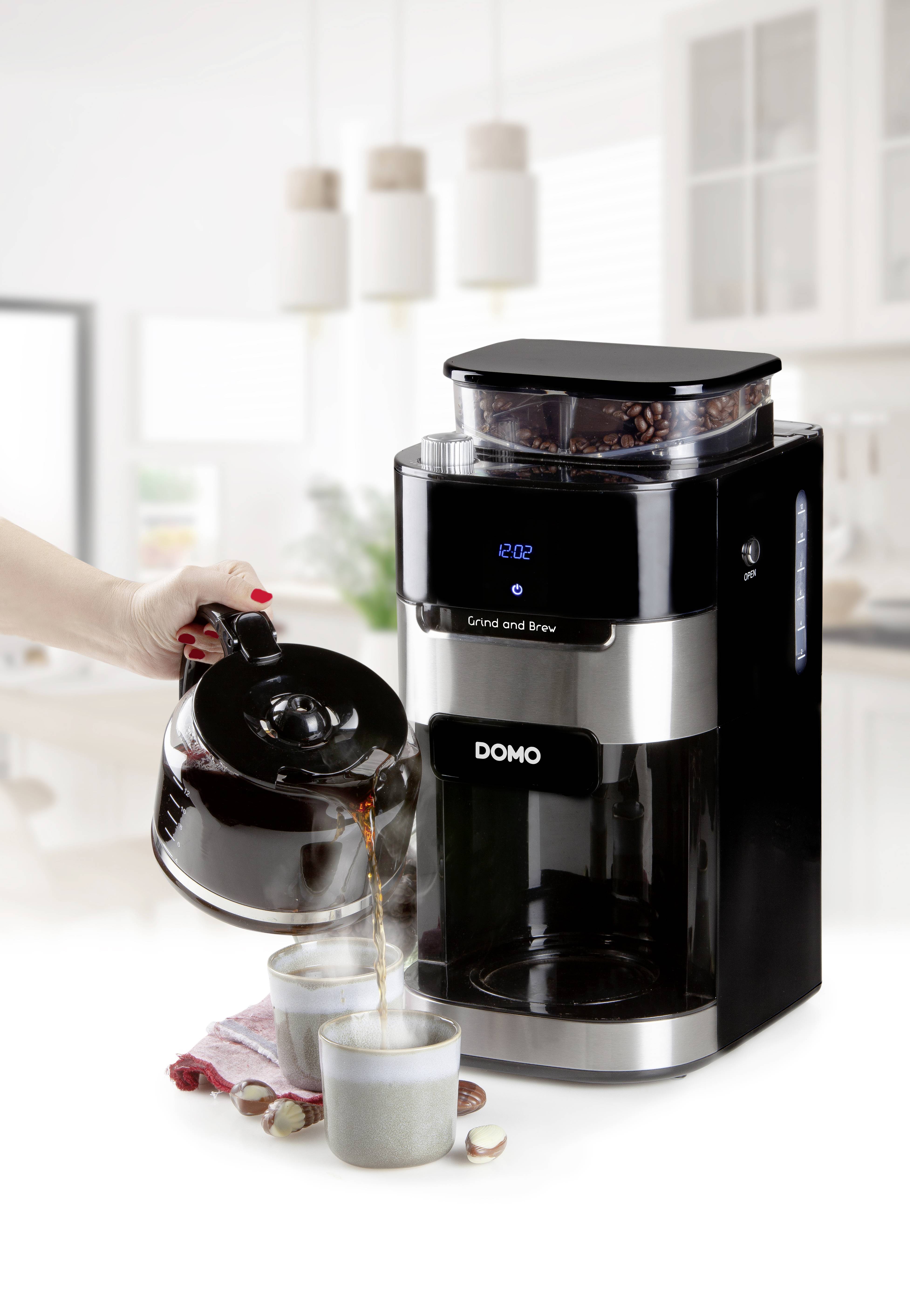 'Eine Kaffeemaschine mit integriertem Mahlwerk; eine Hand gießt frisch gebrühten Kaffee in Tassen. Moderne helle Küchenumgebung.'