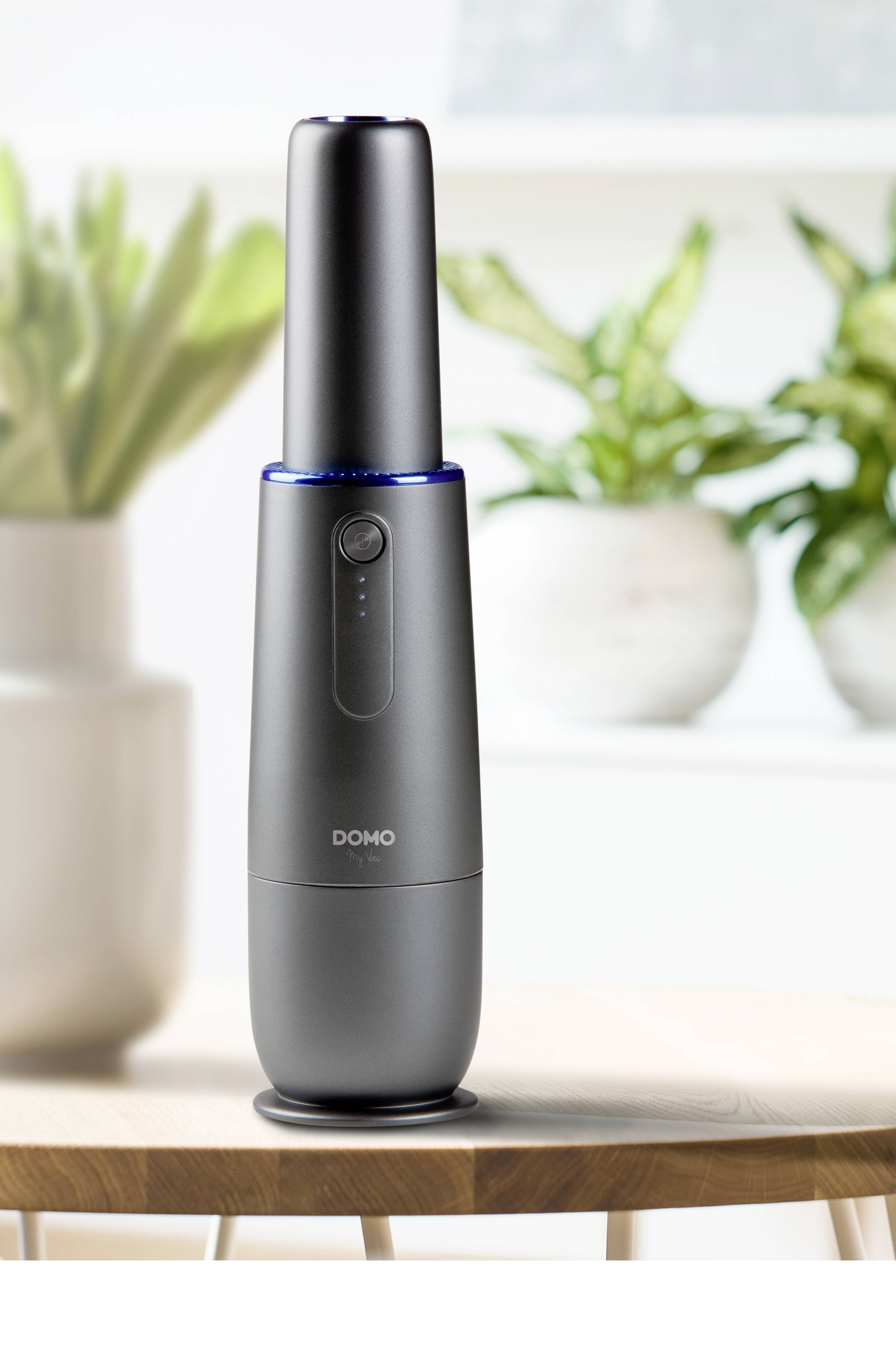 Ein stilvoller, schwarzer Luftreiniger steht auf einem Holztisch. Im Hintergrund sind unscharfe grüne Pflanzen sichtbar.