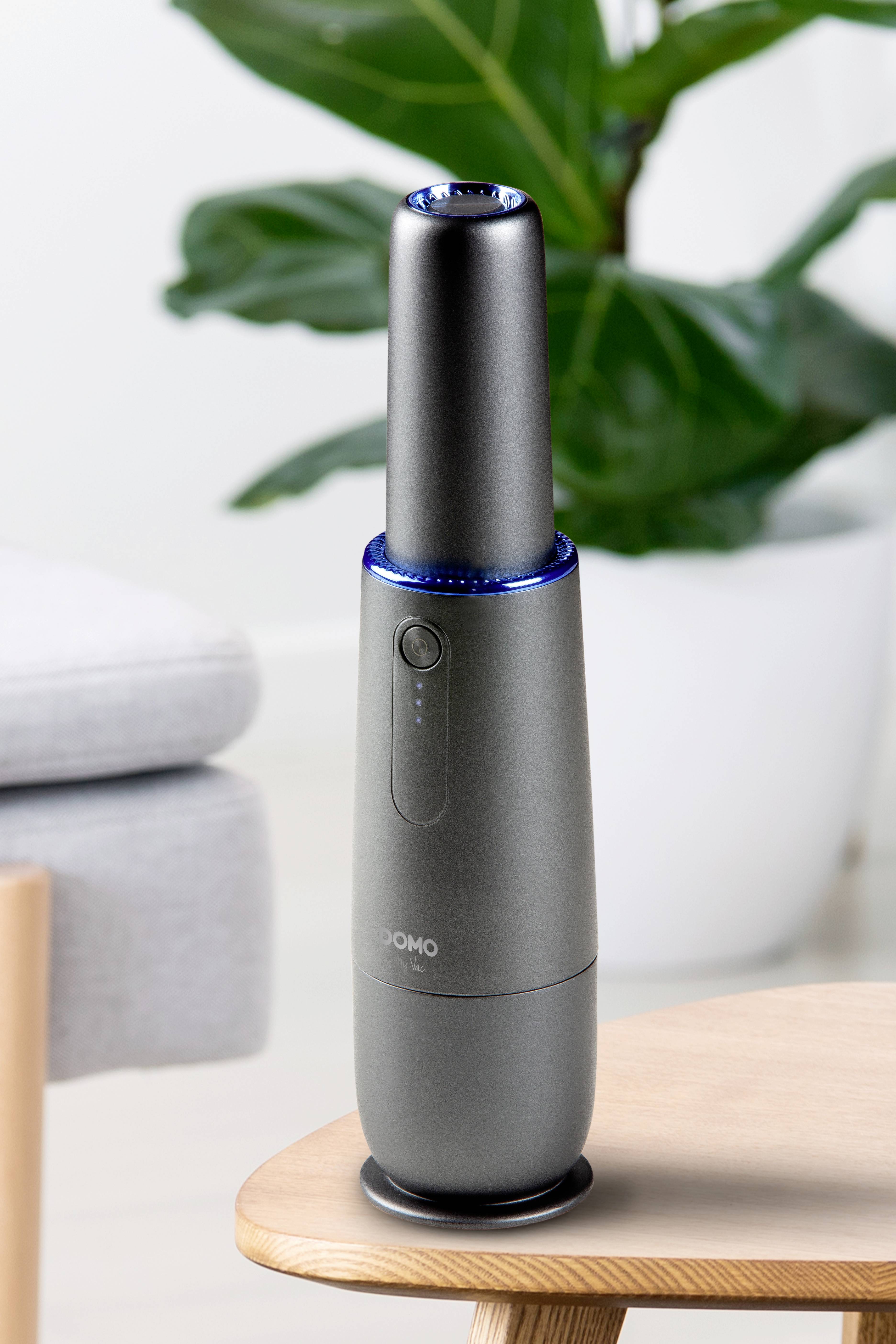 Grauer, schlanker Luftreiniger auf Holztisch im modernen Wohnzimmer, mit blau leuchtendem Ring an der Oberseite.