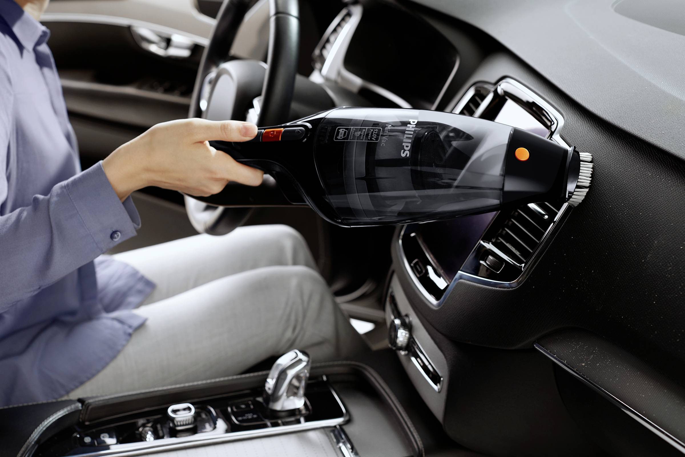 Person benutzt einen Handstaubsauger im Auto, reinigt die Lüftungsschlitze auf dem Armaturenbrett.