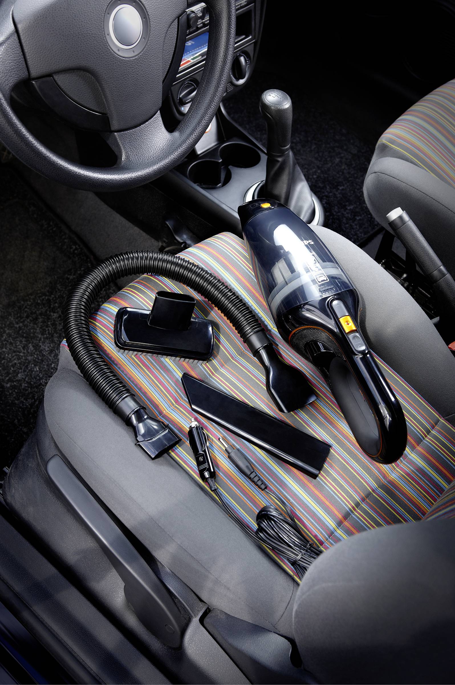 Tragbarer Handstaubsauger mit Zubehör sitzt auf einem bunt gestreiften Autositztbezug, umgeben von Autoinnenraum.