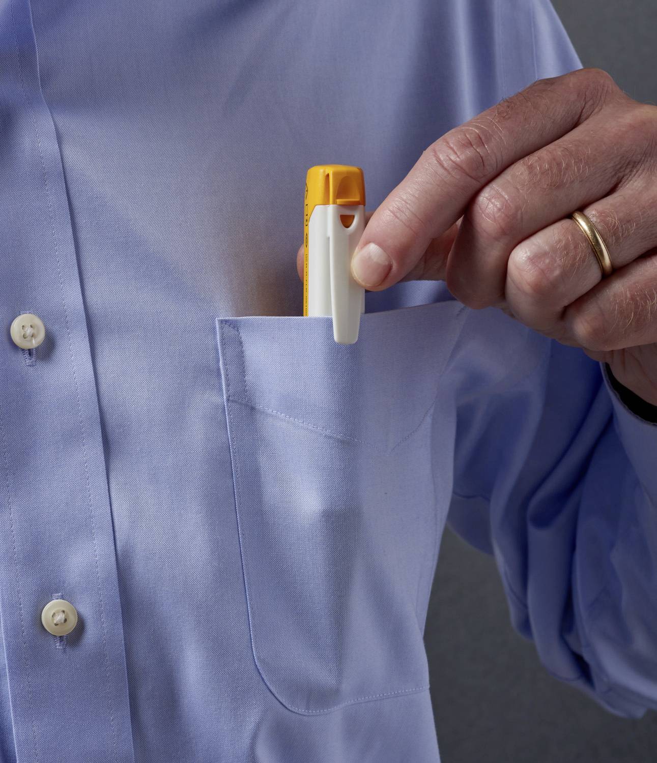 Eine Person steckt einen gelben Inhalator in die Brusttasche eines blauen Hemdes.