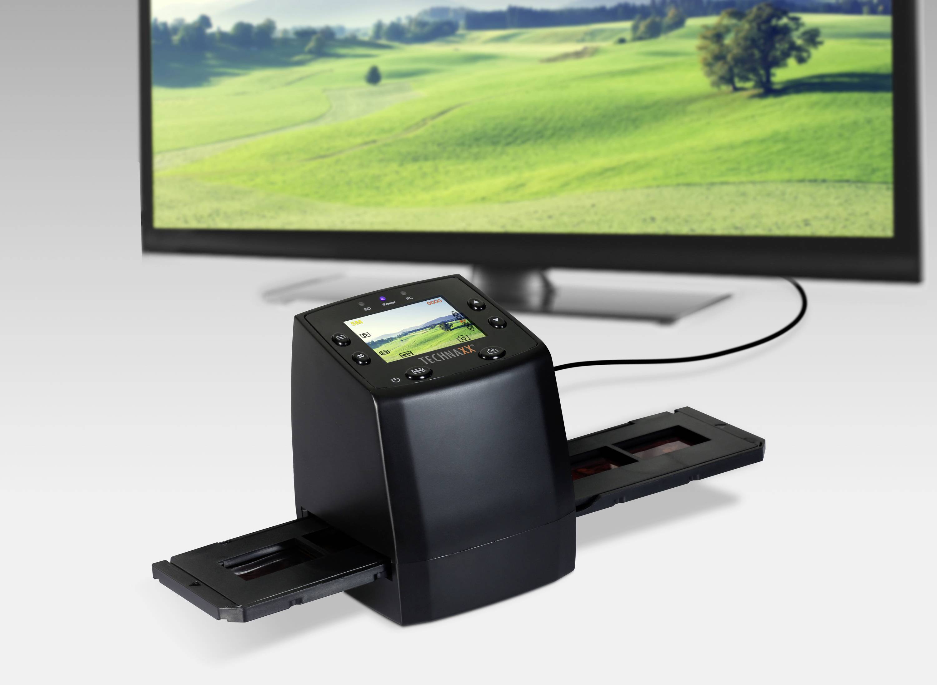 Ein Diascanner digitalisiert Dias, die auf dem Bildschirm angezeigt werden. Im Hintergrund ist eine grüne Landschaft zu sehen.