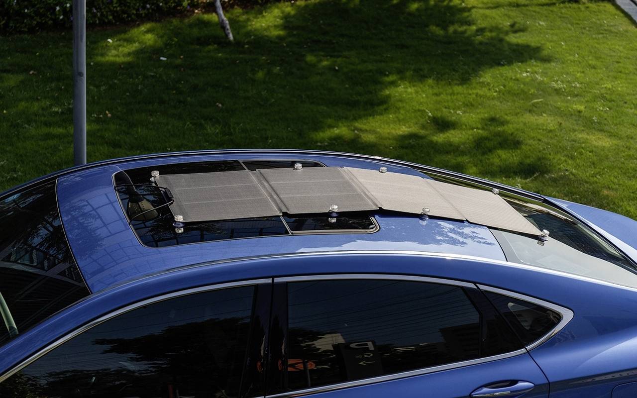 Ein blaues Auto mit einem Solarladegerät auf dem Dach, das auf einer Wiese parkt.