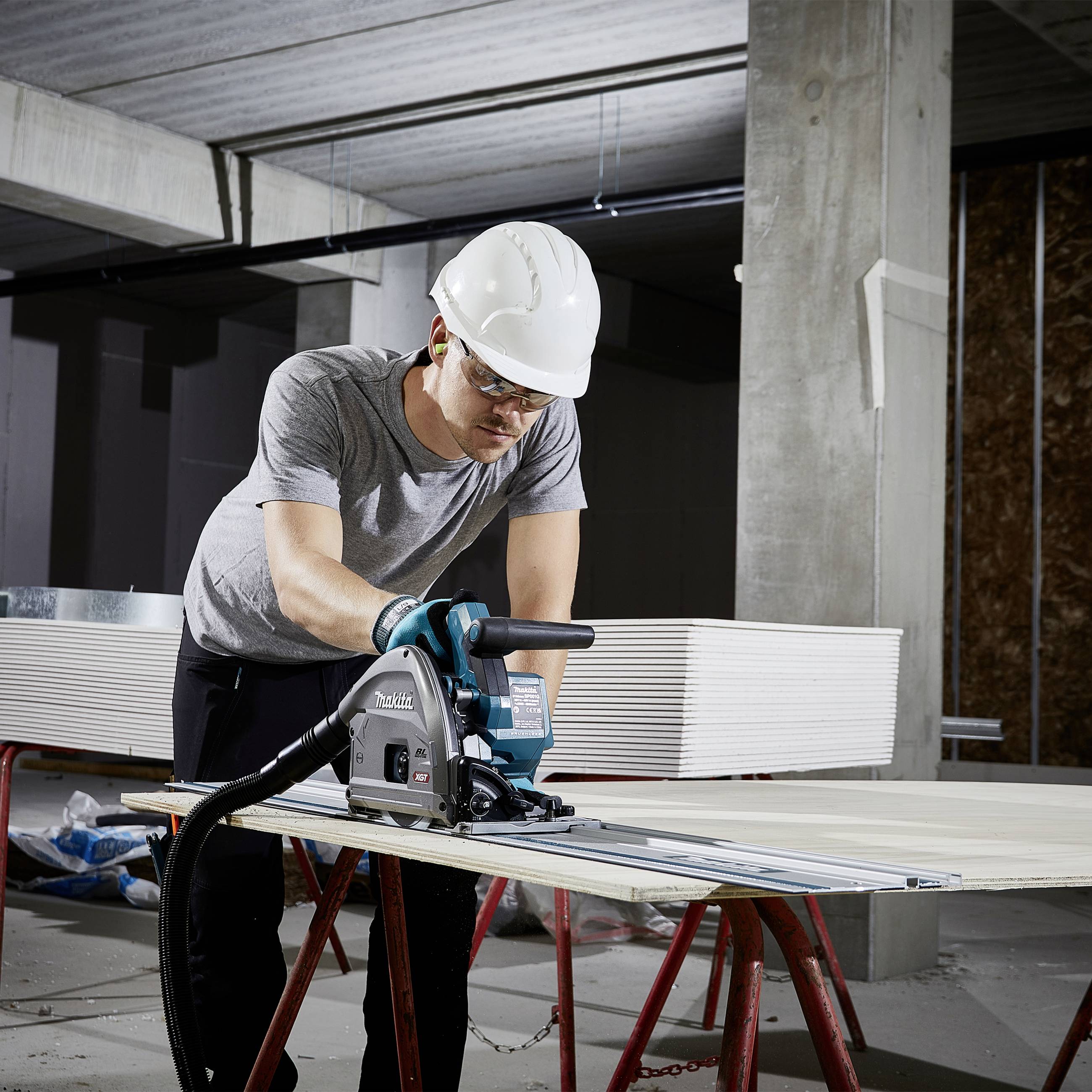 Ein Bauarbeiter mit Schutzhelm schneidet Holzplatten mit einer elektrischen Säge in einem unfertigen Raum.
