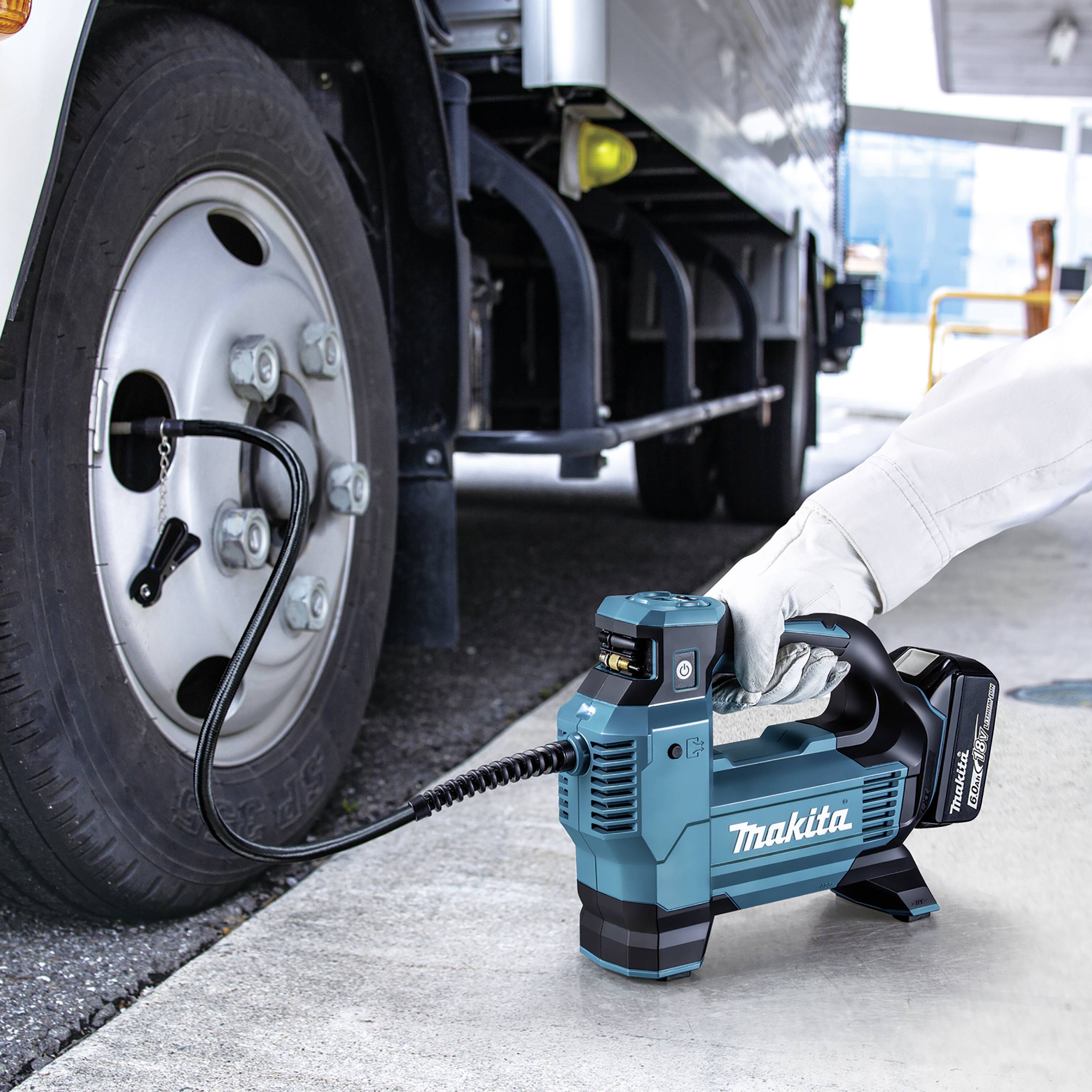 Ein Akkuluftkompressor wird verwendet, um einen Lkw-Reifen aufzupumpen. Eine Hand hält den Kompressor, während er an den Reifen angeschlossen ist.