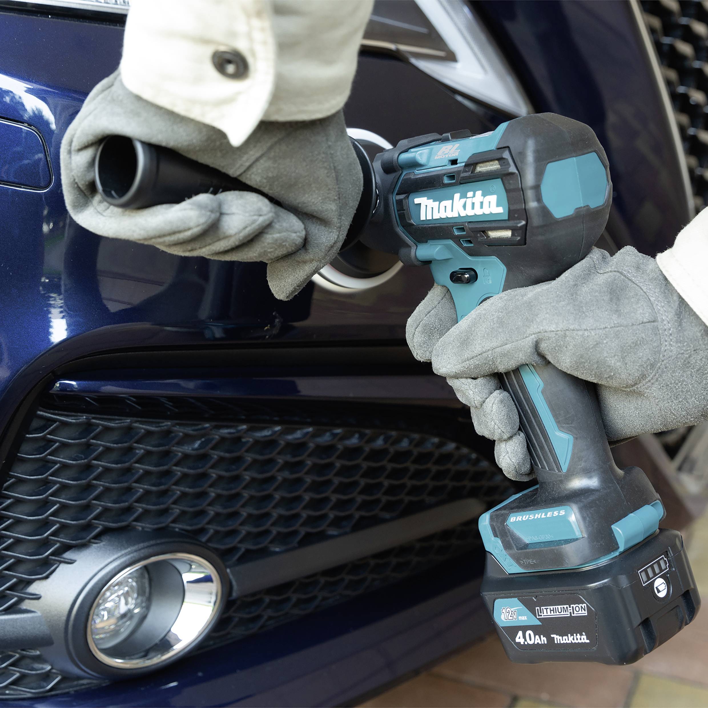 Eine Person in Handschuhen verwendet einen Akkuschrauber, um an einem blauen Auto zu arbeiten. Der Schrauber ist blau und schwarz.