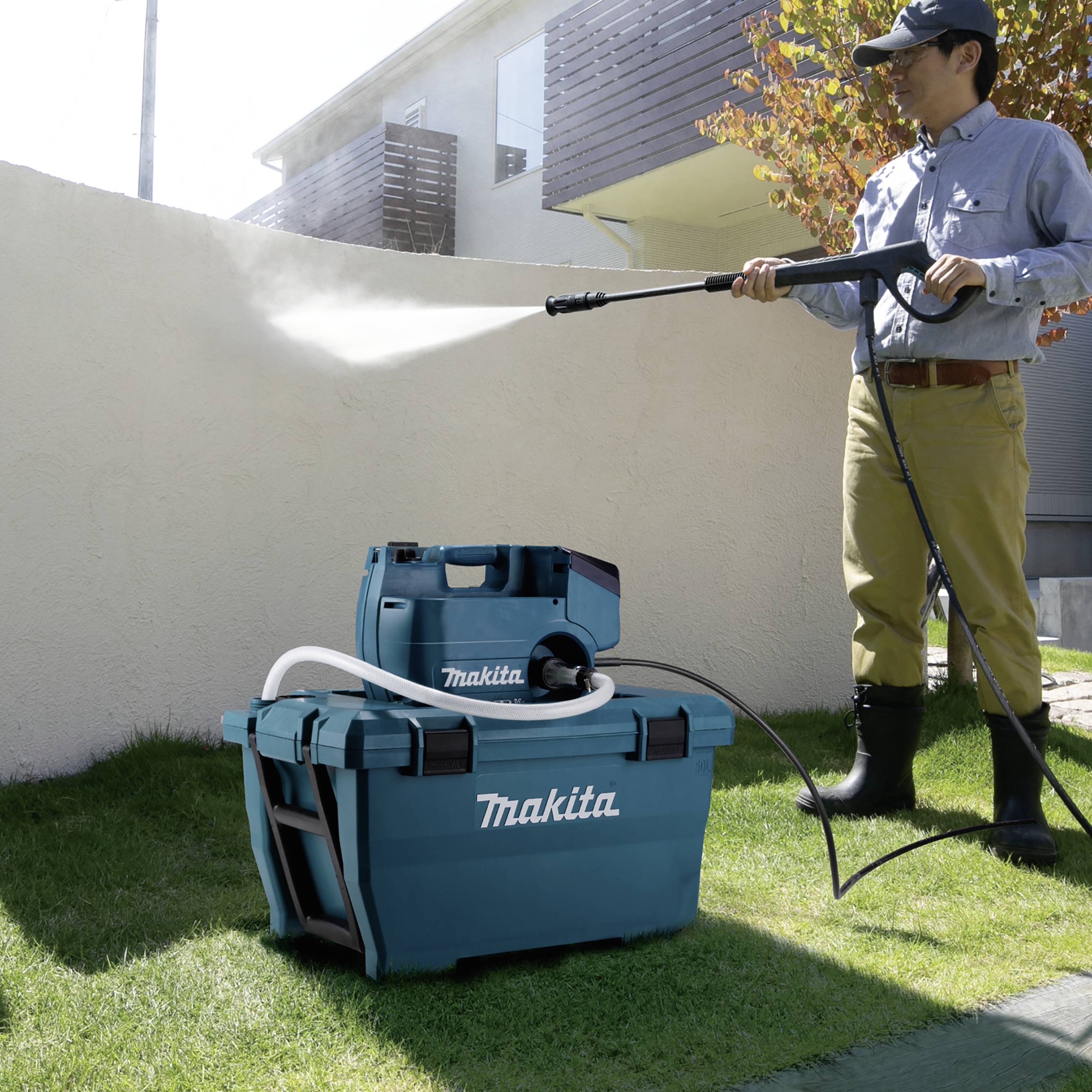 Ein Mann nutzt einen Hochdruckreiniger, um eine Außenwand zu säubern. Vor ihm stehen blaue Reinigungsgeräte auf dem Rasen.