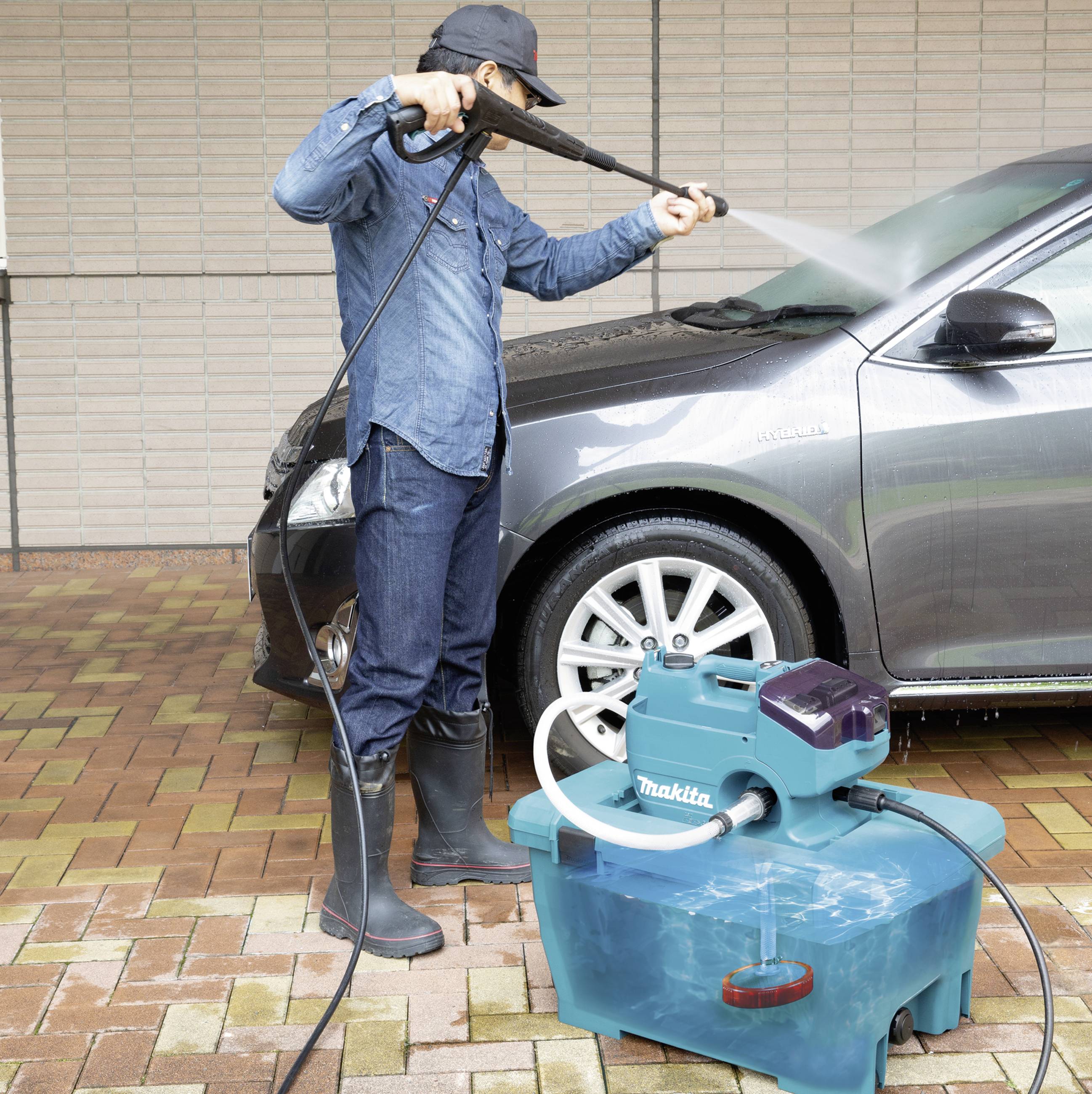 Eine Person wäscht ein Auto mit einem Hochdruckreiniger auf einer gepflasterten Auffahrt. Neben ihnen steht ein Wassersauger.