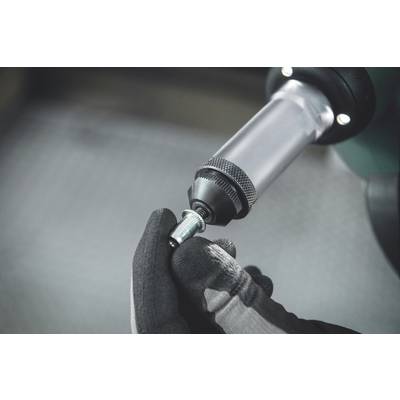 Eine mit Handschuhen bekleidete Hand hält eine kleine Metallkomponente an einen elektrischen Schraubenschlüssel, der gerade benutzt wird.