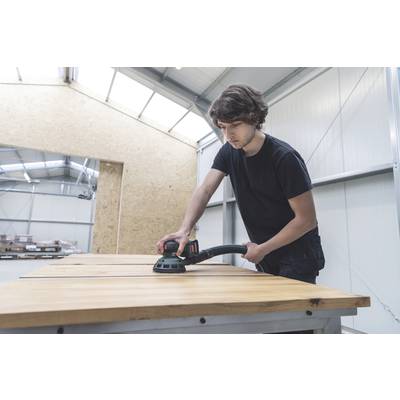 Ein Mann schleift eine große Holzplatte mit einem elektrischen Schleifgerät in einer Werkstatt.