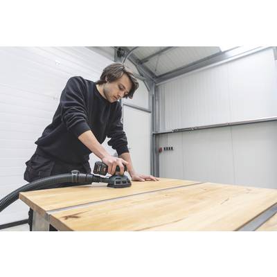 Ein Mann schleift mit einer Schleifmaschine die Oberfläche eines Holztisches in einer Werkstatt.