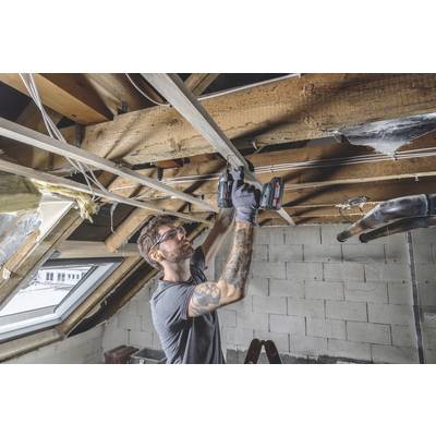 Ein Mann trägt Schutzbrille und Ohrstöpsel, während er unter einem offenen Dachstuhl arbeitet. Er benutzt ein Elektrowerkzeug.