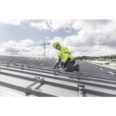 Eine Person in Sicherheitskleidung installiert Solarmodule auf einem großen, silbernen Metalldach. Ein Kran ist im Hintergrund sichtbar.