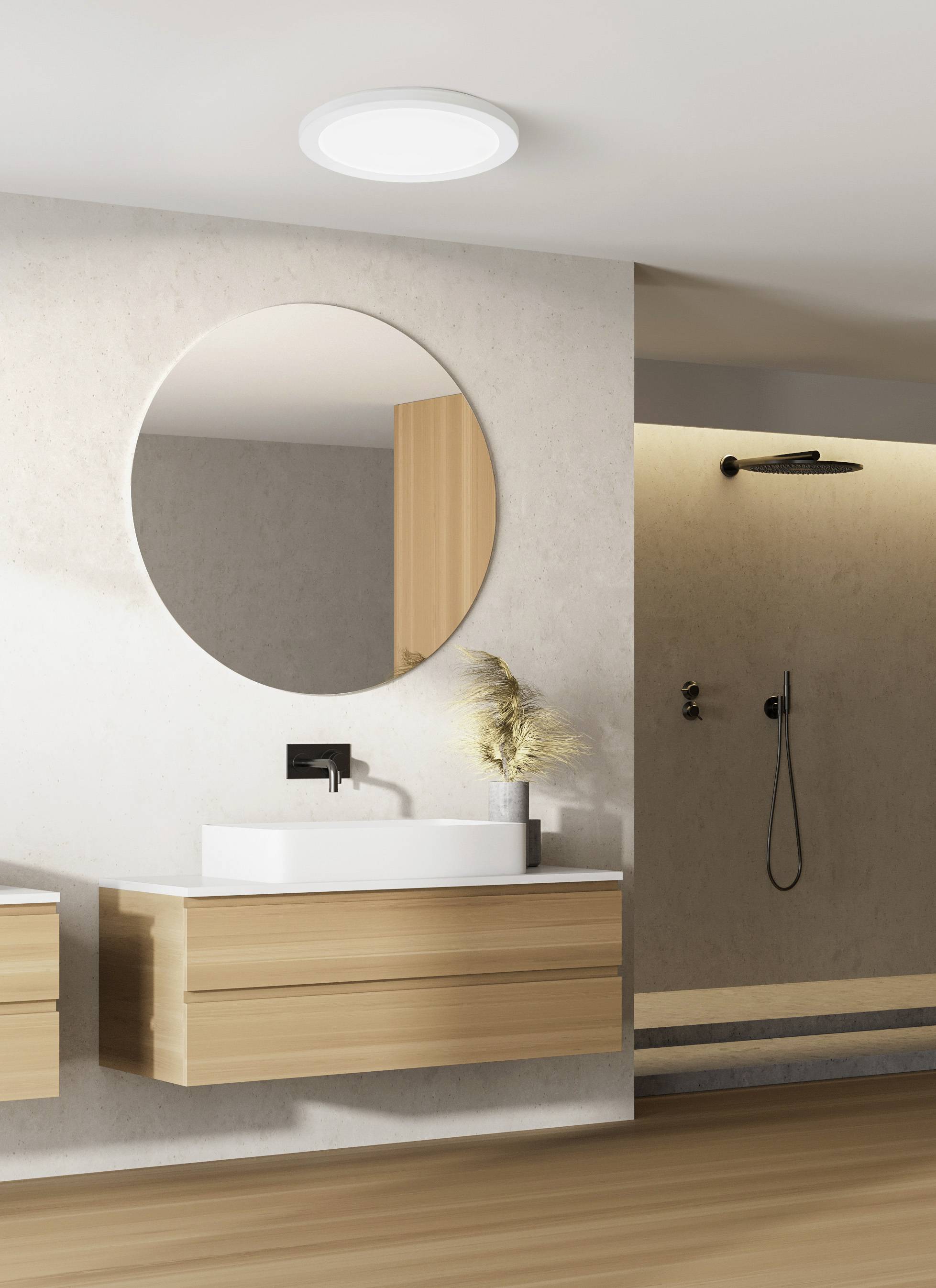 Modernes Badezimmer mit einem runden Spiegel über einem Holzwaschtisch, darauf eine weiße Waschschüssel. Im Hintergrund eine Dusche.