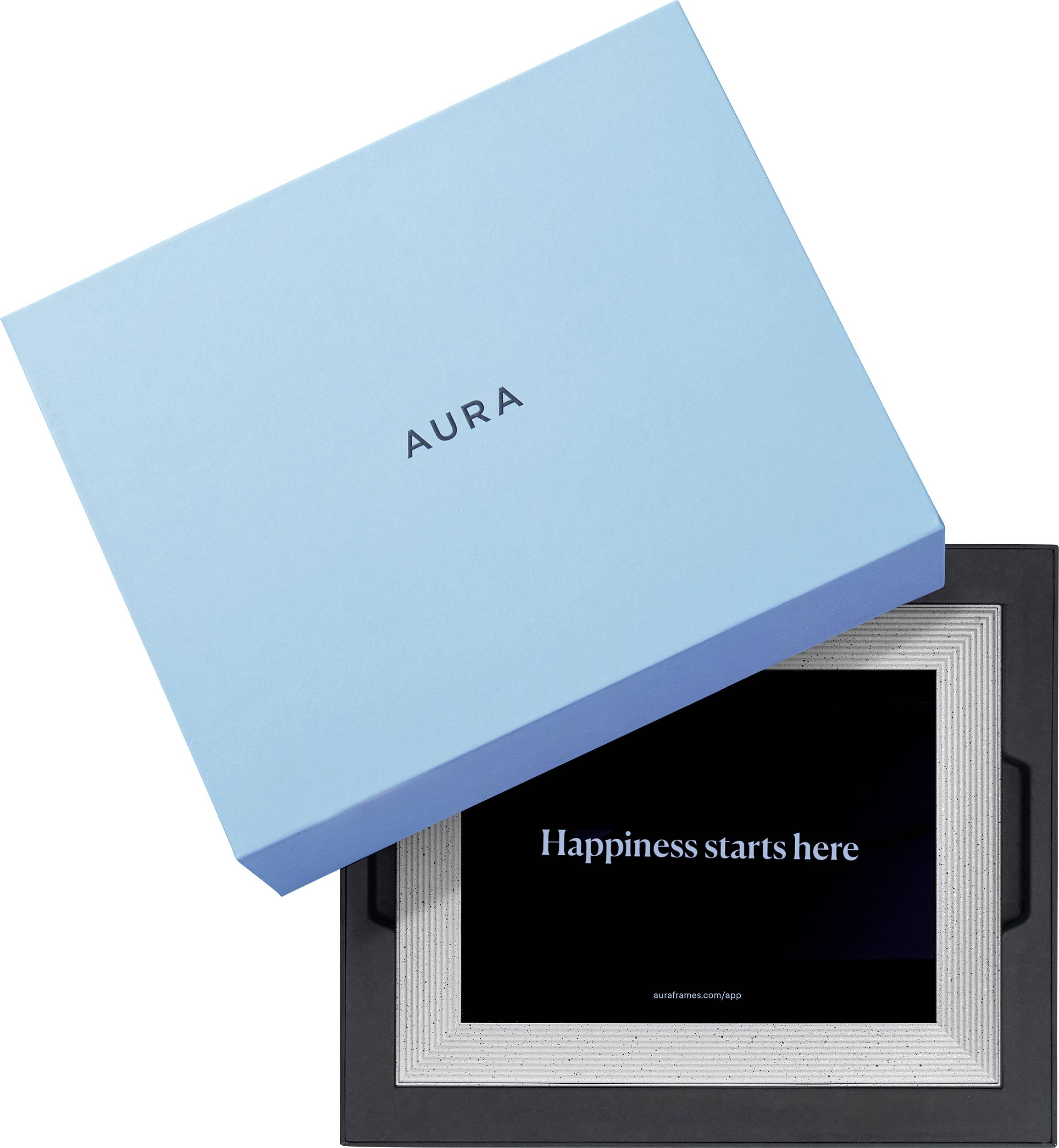 Eine geöffnete blaue Box mit der Aufschrift 'AURA' zeigt einen schwarzen Bilderrahmen mit dem Schriftzug 'Happiness starts here'.
