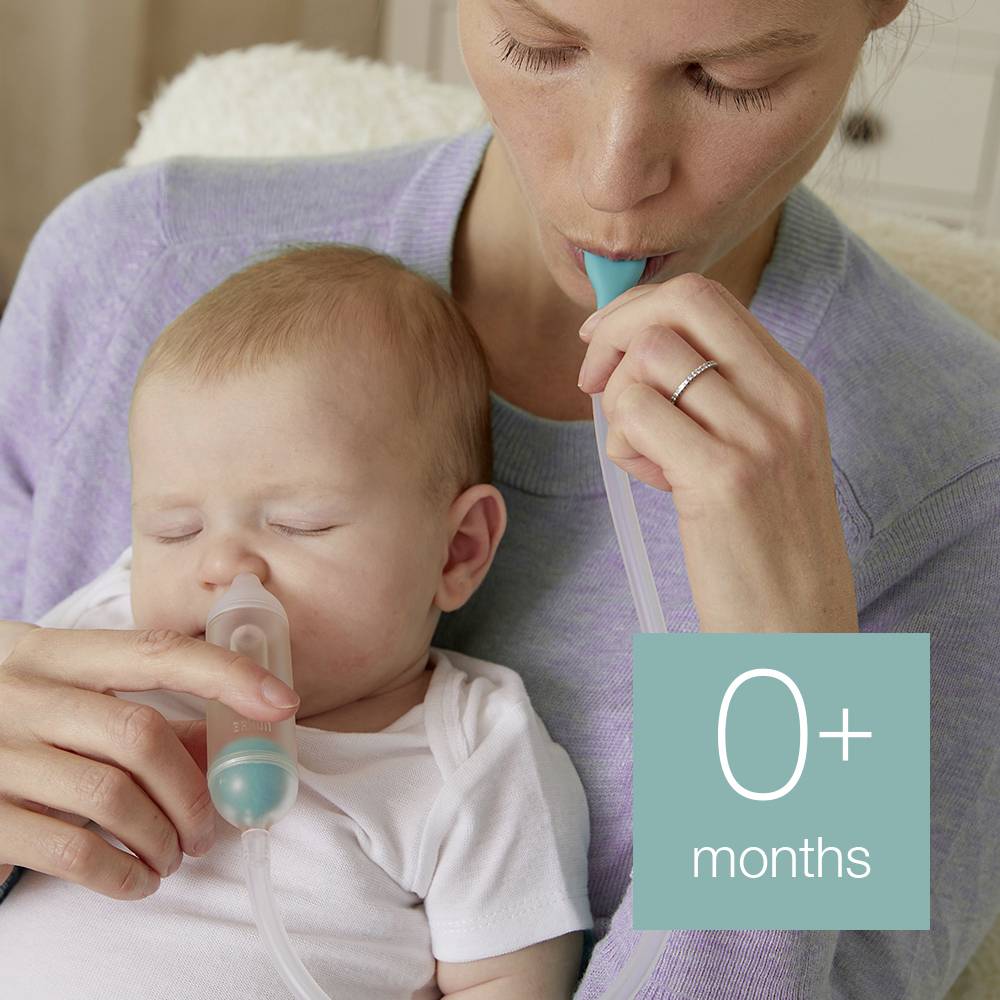 Eine Mutter benutzt einen Nasensauger, um das Baby von Schnupfen zu befreien. Das Baby schläft dabei ruhig. Links unten steht '0+ Monate'.