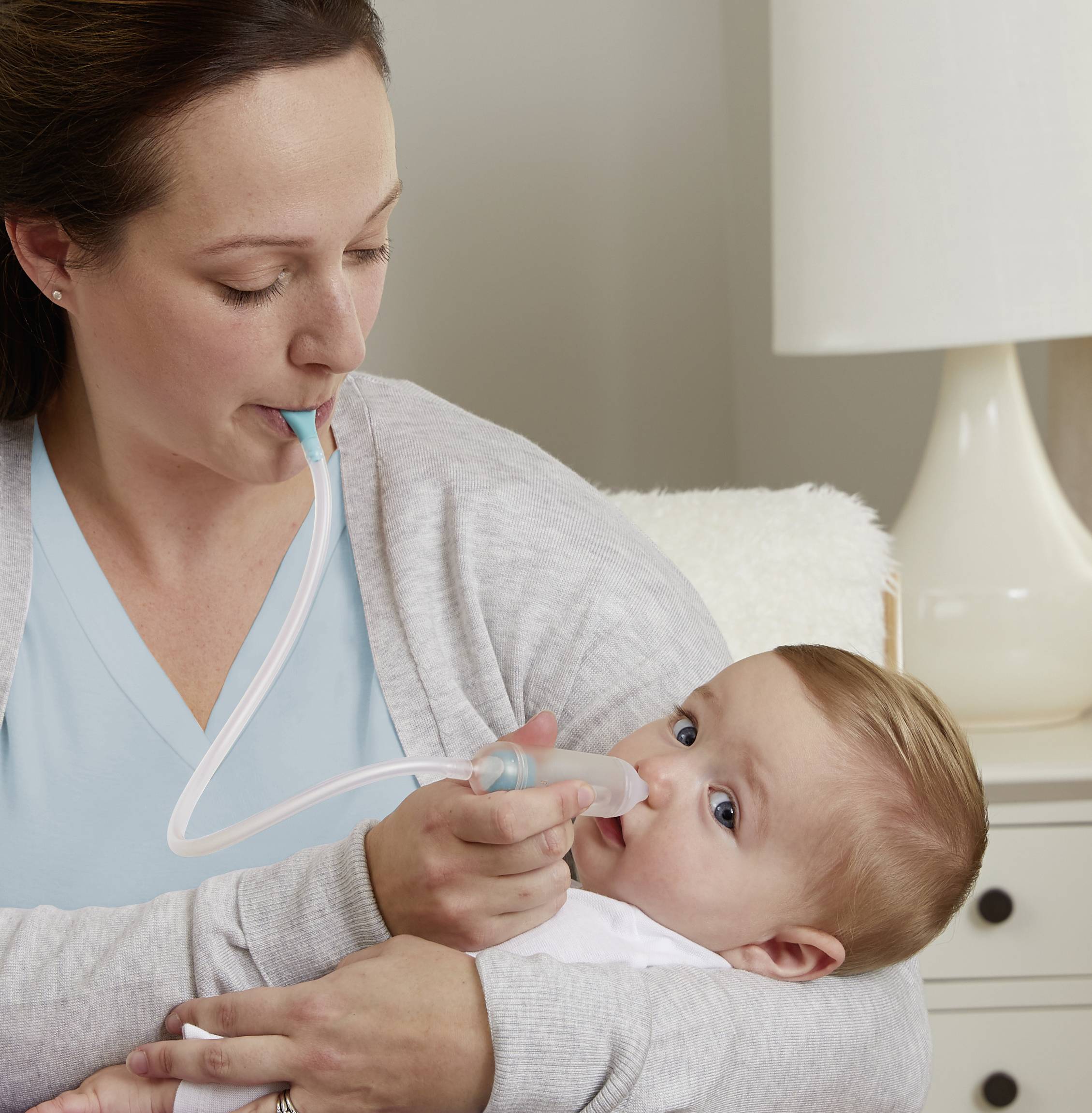 Eine Frau hält ein Baby und nutzt einen Nasensauger, um die Nase des Babys zu reinigen. Das Baby liegt entspannt auf ihrem Arm.