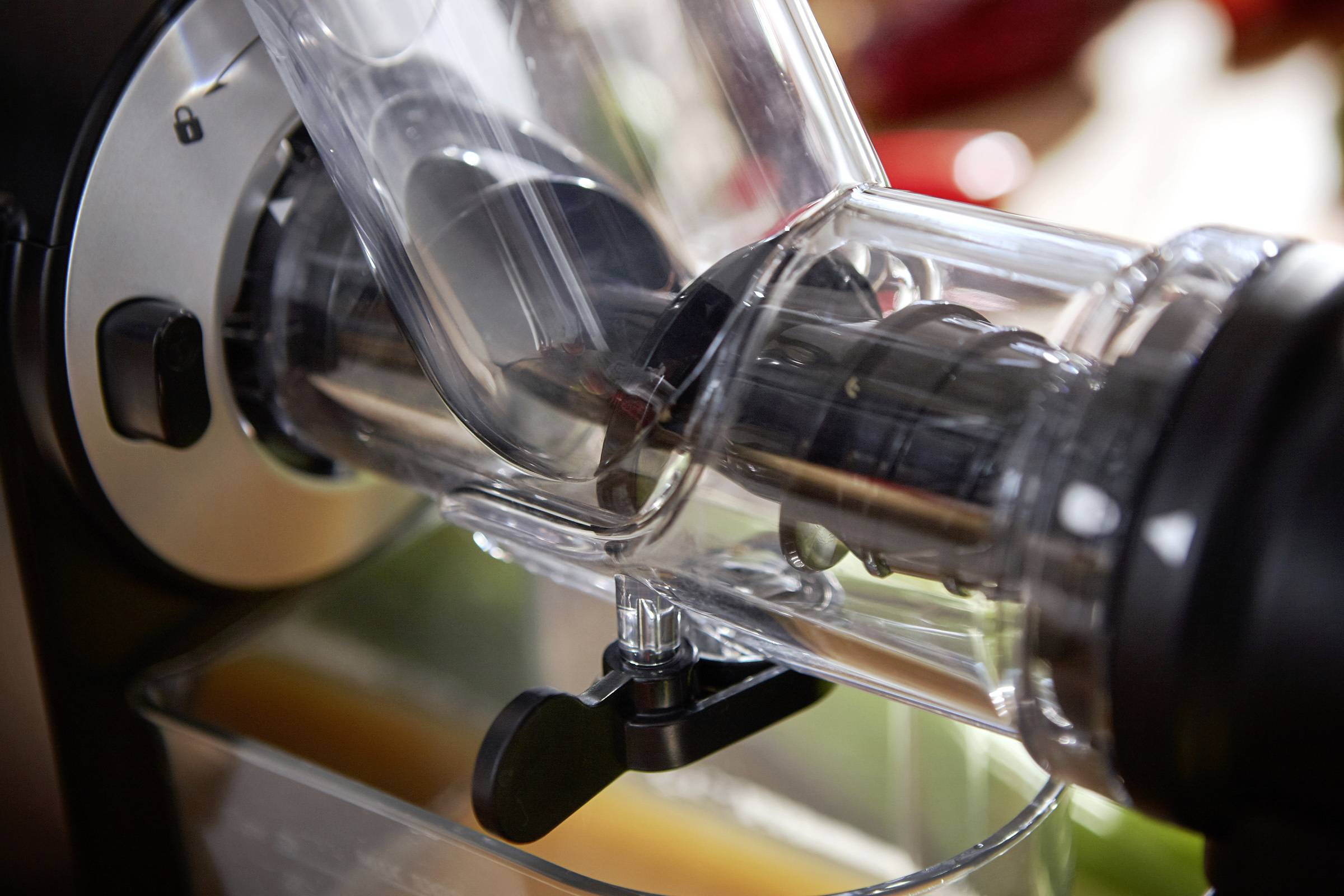 'Nahaufnahme eines Entsafters während des Gebrauchs. Klarer Plastikbehälter mit Saftauslauf. Frisches Obst wird zu Saft verarbeitet.'