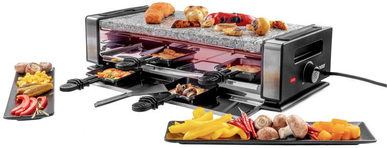 Ein Raclette-Grill mit heißer Steinplatte und darunterliegenden Pfännchen. Auf dem Grill liegen verschiedene Speisen wie Brot und Gemüse.