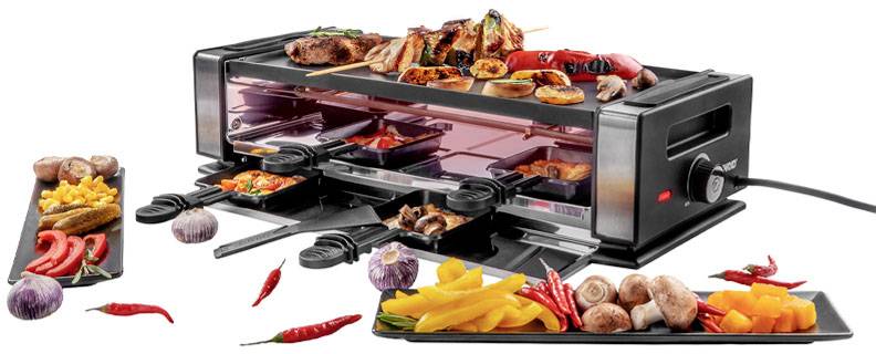 Raclette-Grill mit verschiedenen Speisen: Gemüse, Pilze, Fleischspieße und Chili. Auf dem Tisch liegen weitere Teller mit Zutaten.