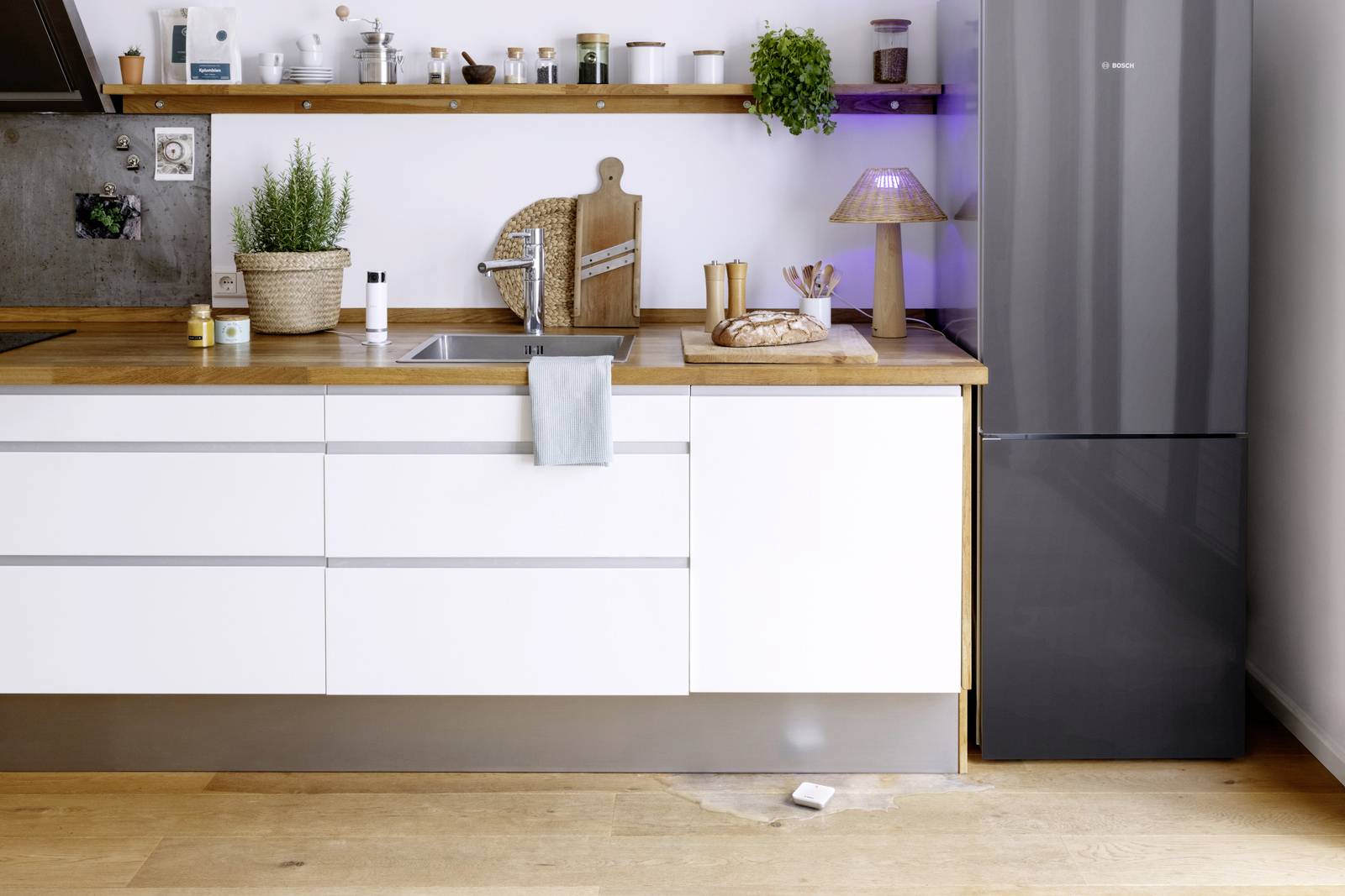 Moderne Küche mit weißen Schränken, brauner Arbeitsplatte, Spüle und Küchengeräten. Pflanzen und Accessoires dekorieren das Regal.