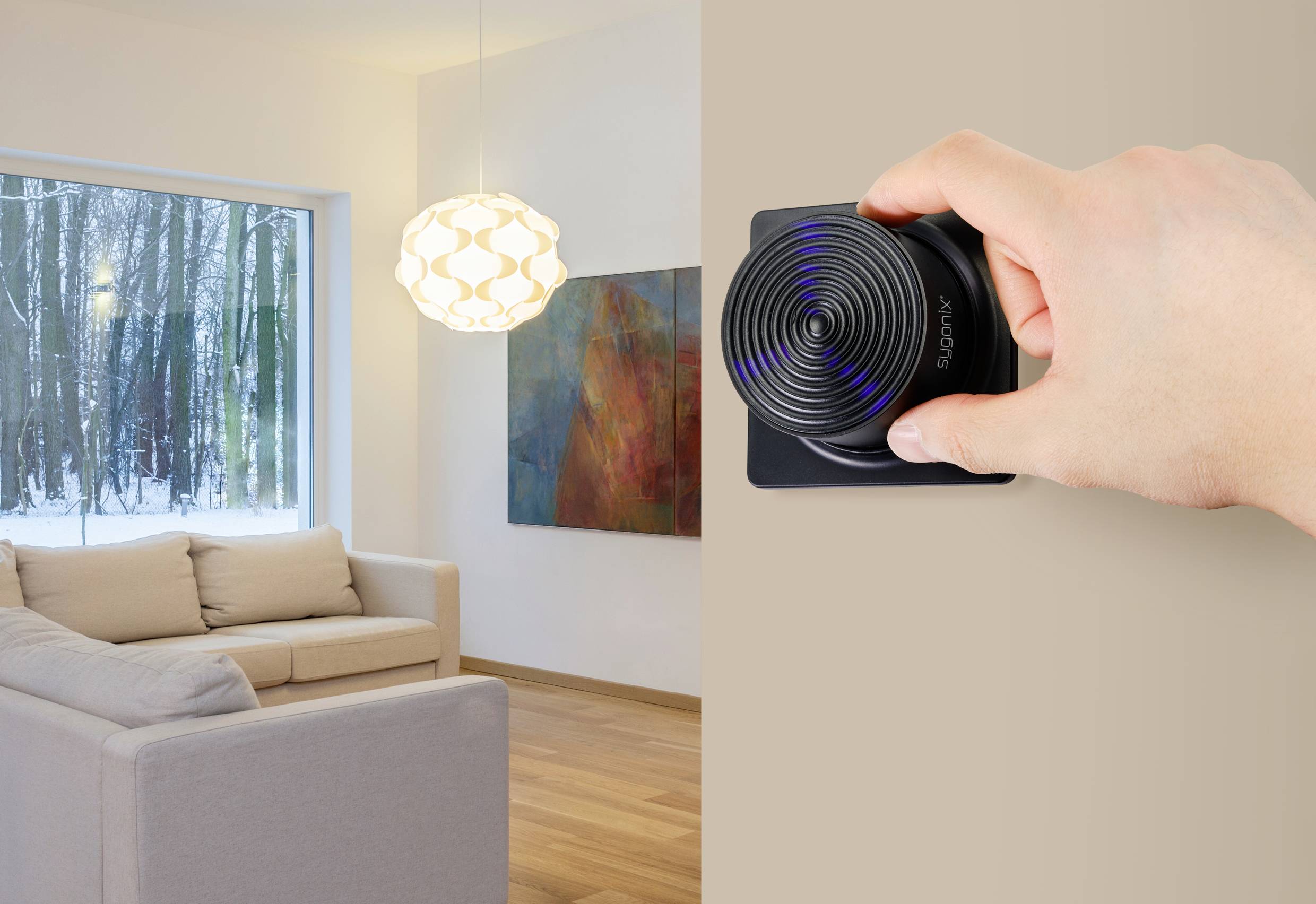 Eine Hand bedient ein modernes, rundes Thermostat an der Wand eines stilvollen Wohnzimmers mit Sofa, Holzfußboden und großen Fenster.