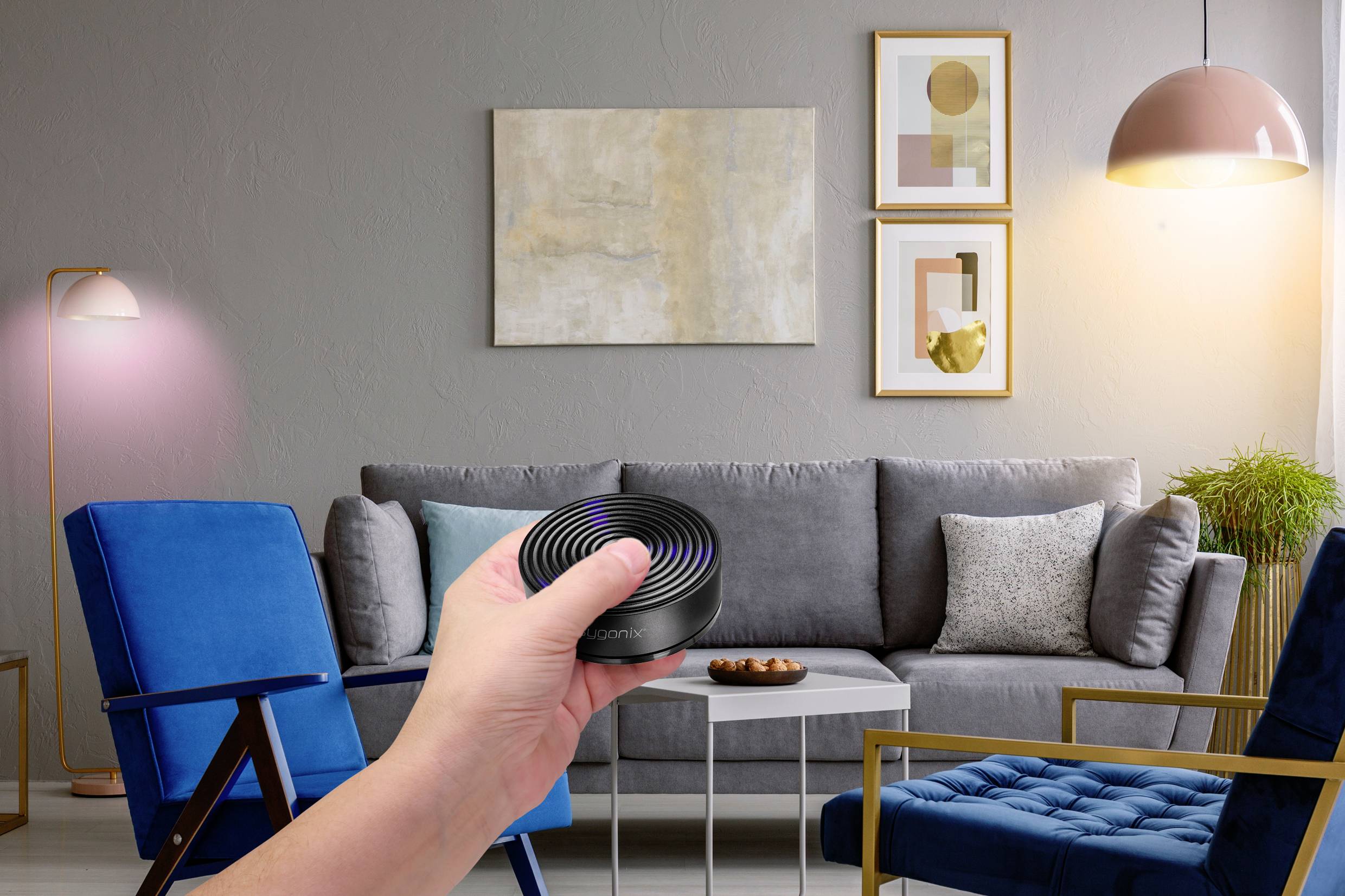 Eine Hand hält einen Smart-Home-Controller in einem modernen Wohnzimmer mit grauem Sofa, blauen Sesseln und dekorativer Beleuchtung.