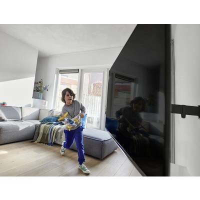 Ein Kind rennt durch ein Wohnzimmer mit einem Spielzeug in der Hand. Im Hintergrund sind ein Sofa, ein Tisch und große Fenster zu sehen.