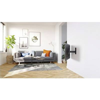 Moderner, heller Wohnraum mit grauem Sofa, bunten Kissen und Pflanzen. An der Wand ein montierter Bildschirm. Holzboden und große Fenster.
