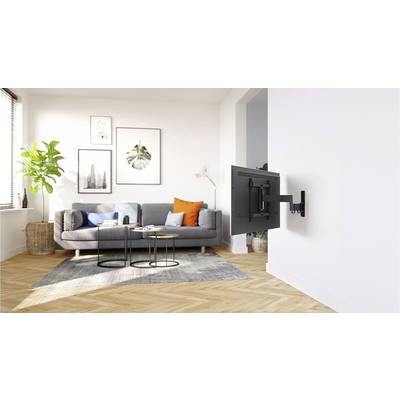 Helles Wohnzimmer mit grauem Sofa, bunten Kissen, Pflanzen, und einem an der Wand montierten Fernseher auf einem schwenkbaren Arm.