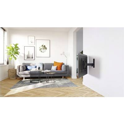 Helles Wohnzimmer mit grauem Sofa, bunte Kissen, Zimmerpflanze, Wandbildern und einem an der Wand montierten Fernseher.