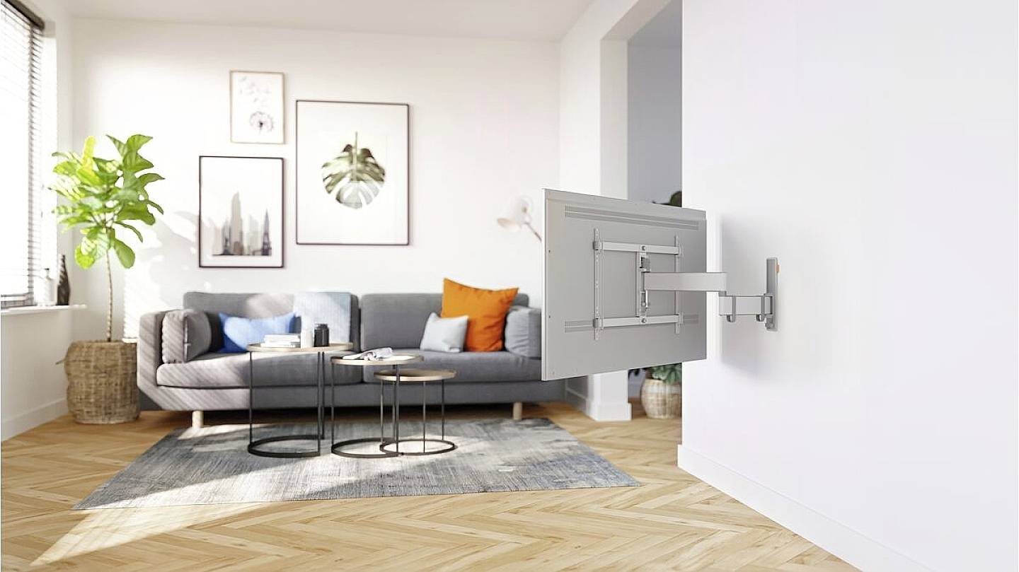 Ein modernes Wohnzimmer mit einem Sofa, zwei runden Tischen, Wandkunst und einer Pflanze. An der Wand ist eine ausziehbare TV-Halterung montiert.