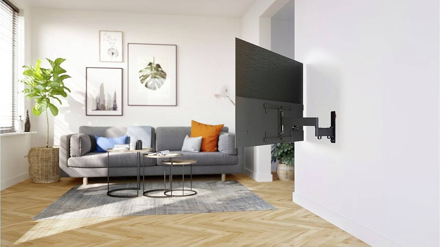 'Wandhalterung mit schwenkbarem Flachbildfernseher in modernem Wohnzimmer mit grauem Sofa, Pflanzen und hellem Holzfußboden.'