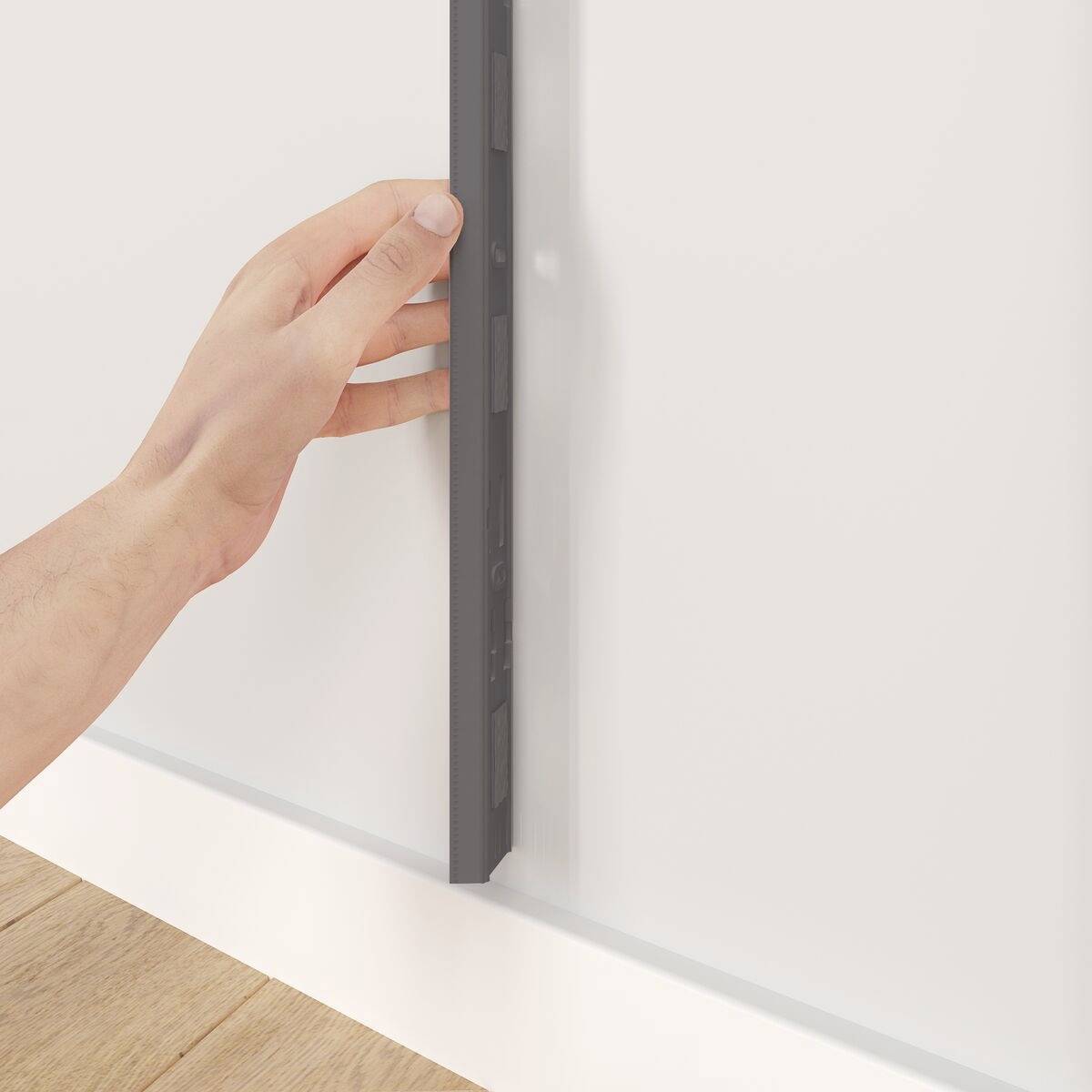 Eine Hand berührt die Kante eines schmalen schwarzen Geräts, das an der Wand montiert ist. Im Hintergrund ist ein Holzfußboden sichtbar.