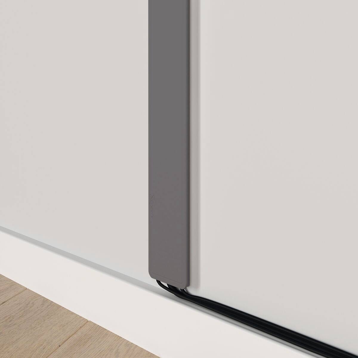 Ein dunkelgrauer Kabelkanal verläuft senkrecht an einer weißen Wand und verdeckt Kabel. Er sorgt für eine ordentliche Optik im Raum.
