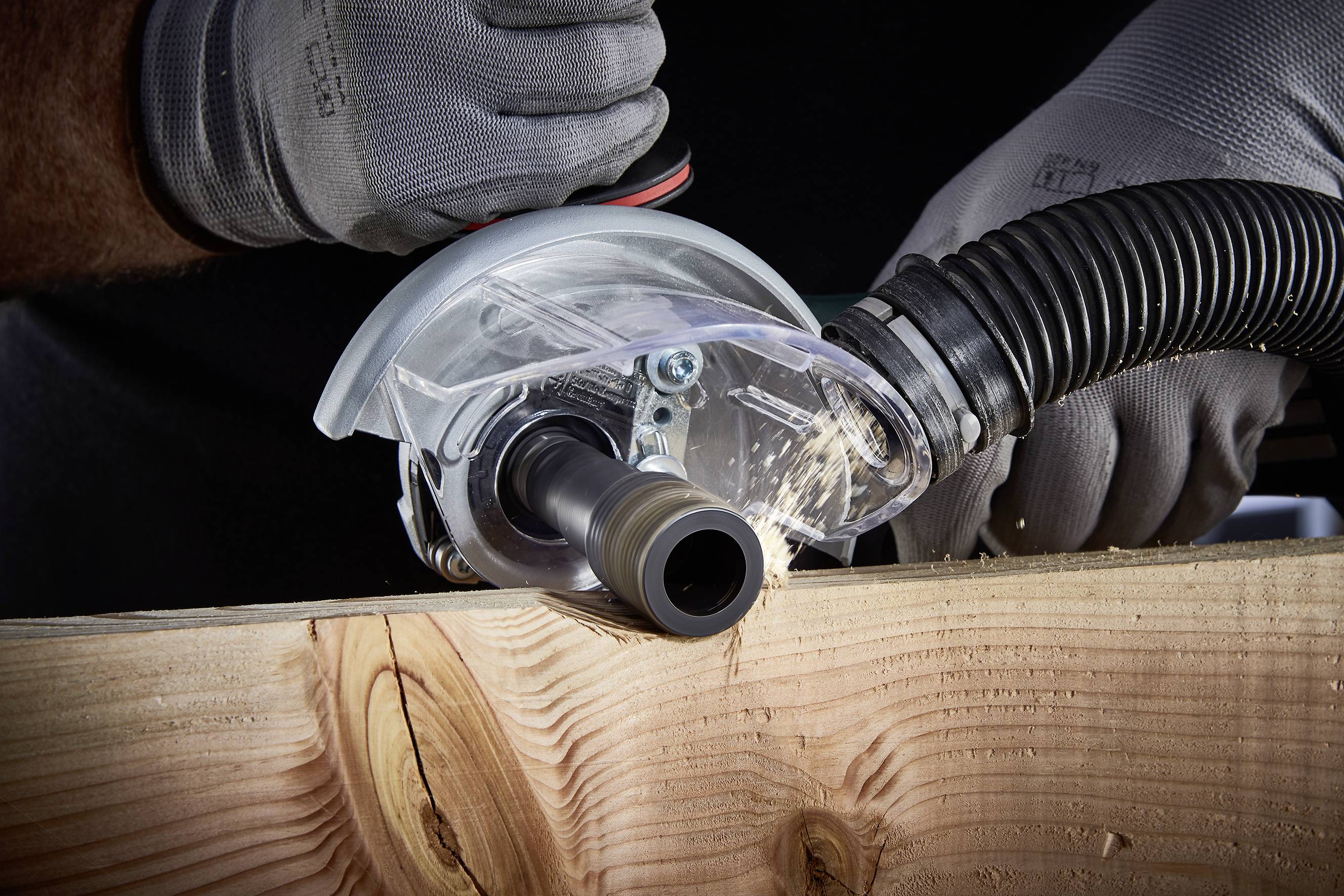 'Ein Handwerker schneidet ein Holzbrett mit einer Kreissäge. Funken fliegen von der Klinge. Schutzhände und Staubsaugerschlauch sind sichtbar.'