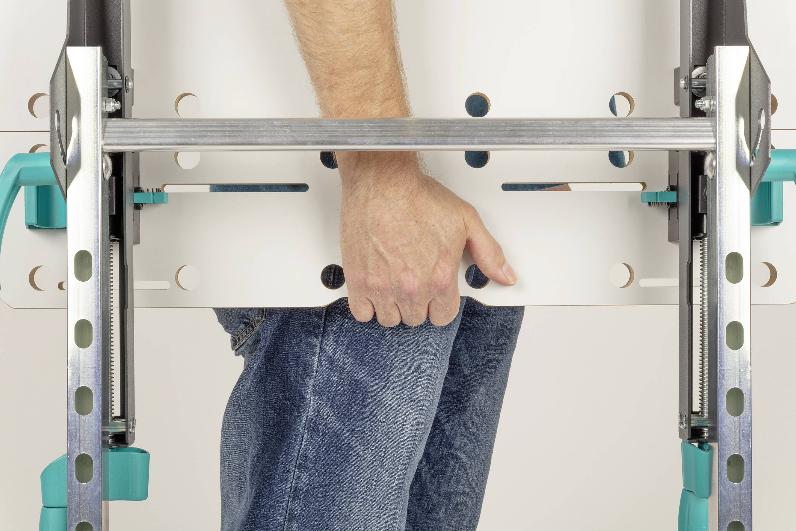 Eine Person hält eine Metalllatte mit der Hand, gekleidet in blaue Jeans. Die Latte scheint Teil eines Arbeitsgeräts zu sein.